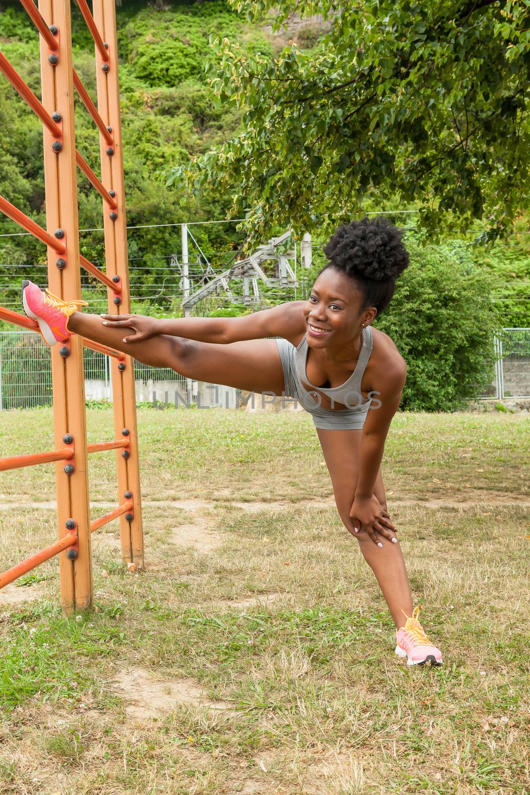 African young woman doing stretching exercises in urban structures for sports in a city park