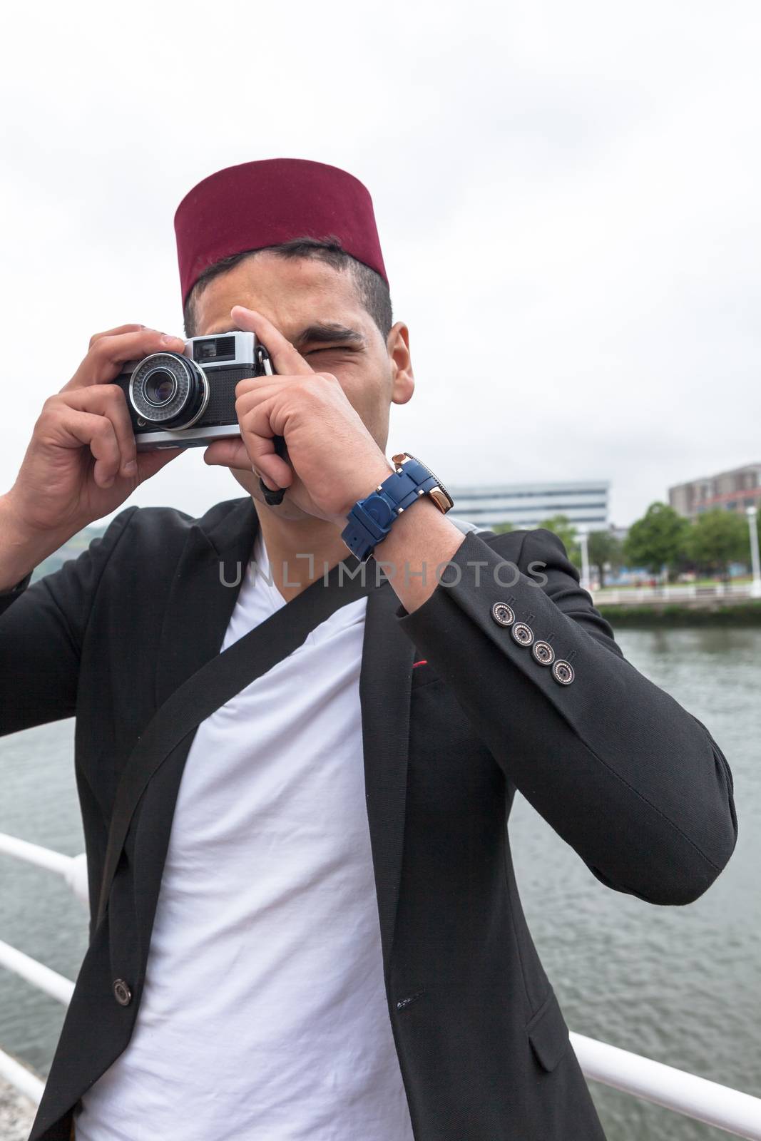 Modern muslim younger with a fez cap shooting through his vintage film camera