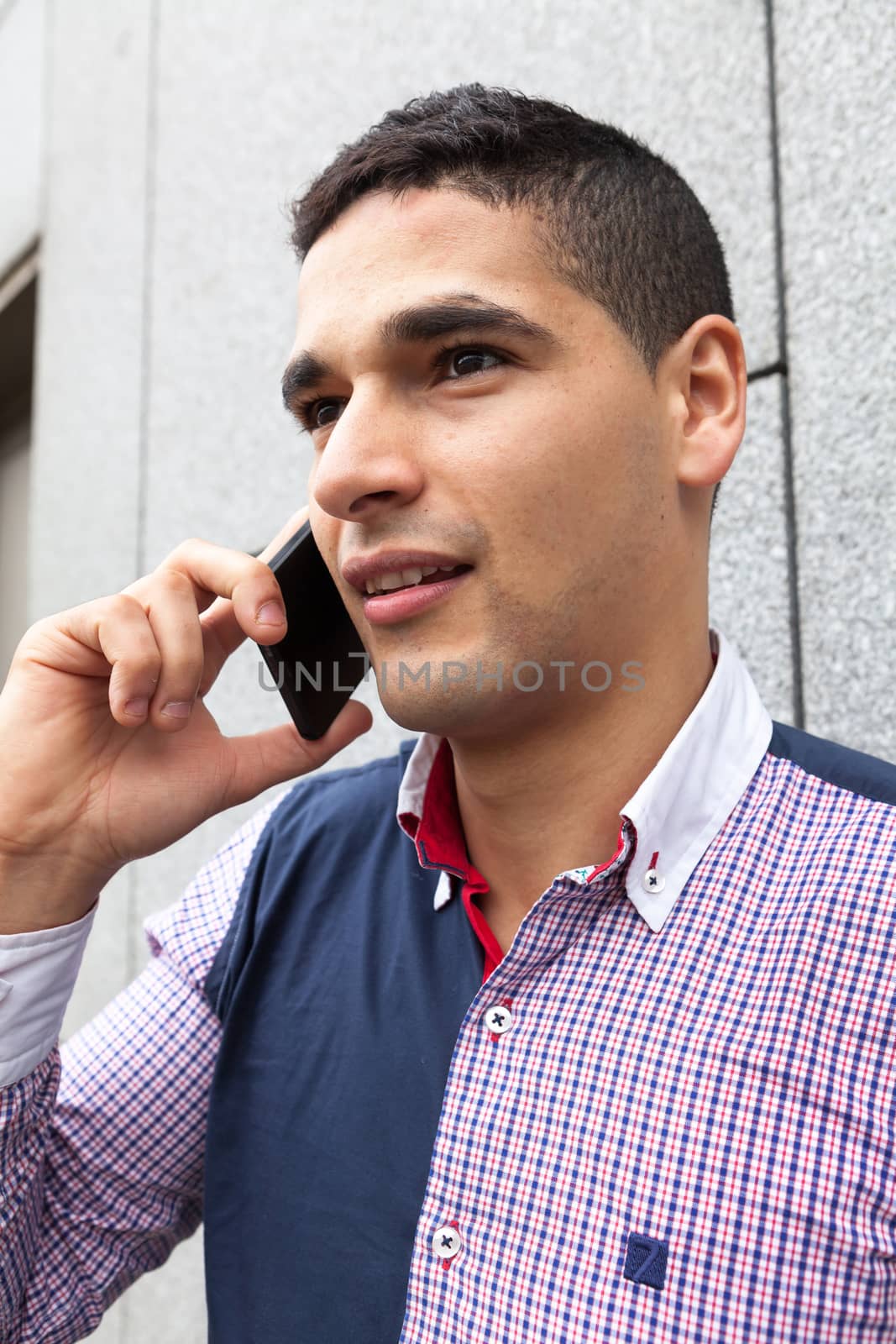 Young arab man talking on the phone next to a stone wall