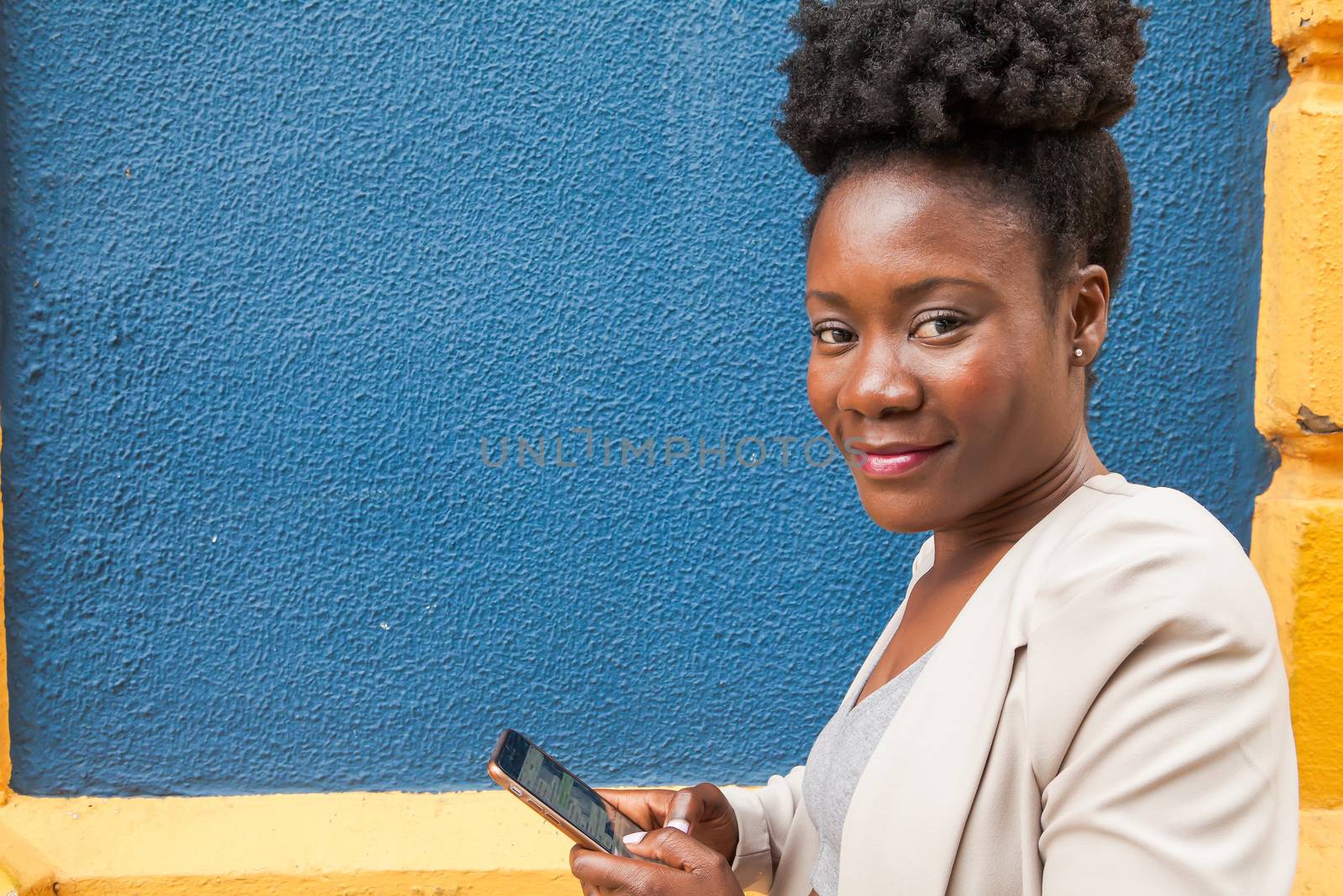 Medium shot of an african young woman in sportswear looking at his mobile phone with a colorful wall blue and yellow