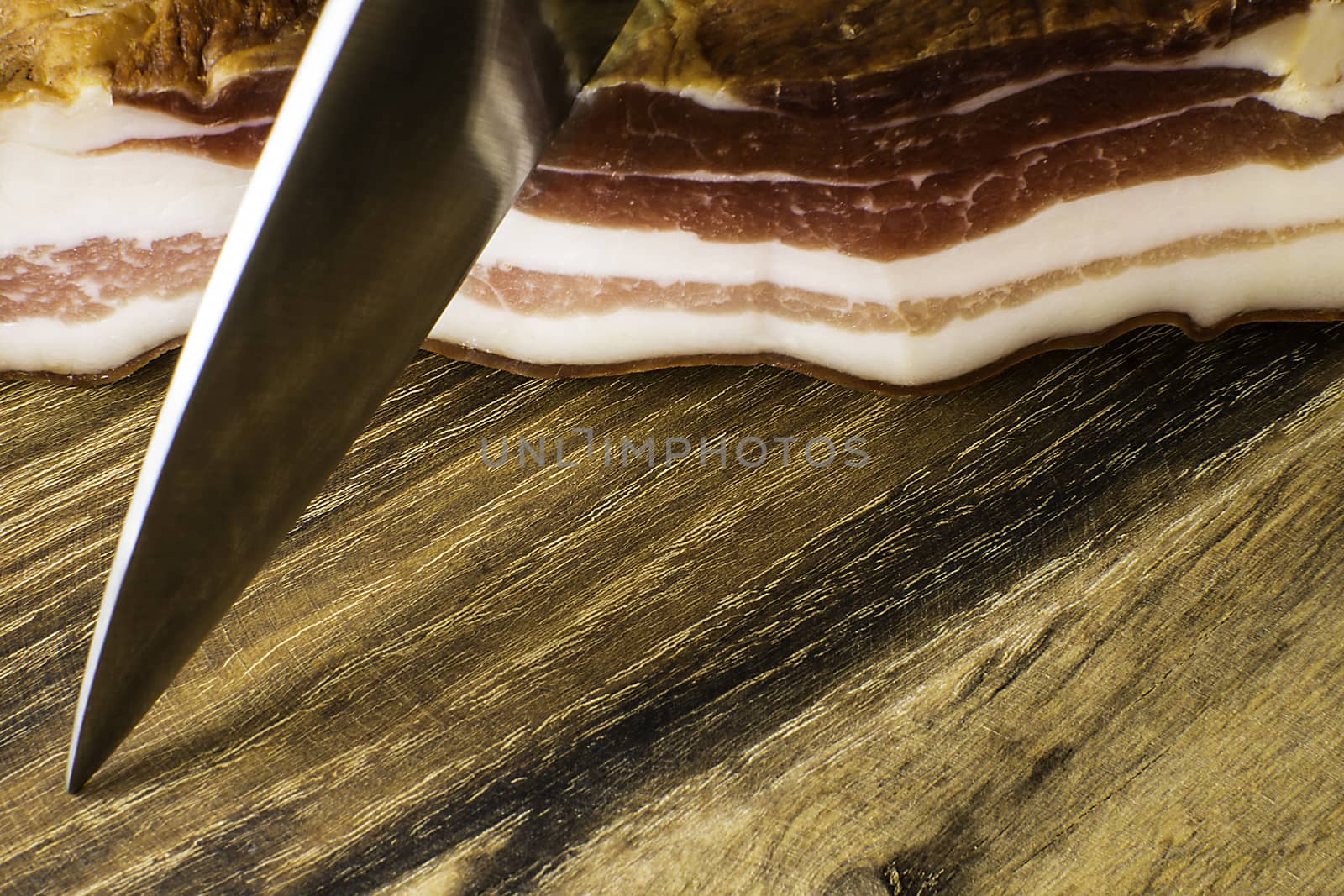 Smoked bacon on vintage wooden board with a knife ready to cut