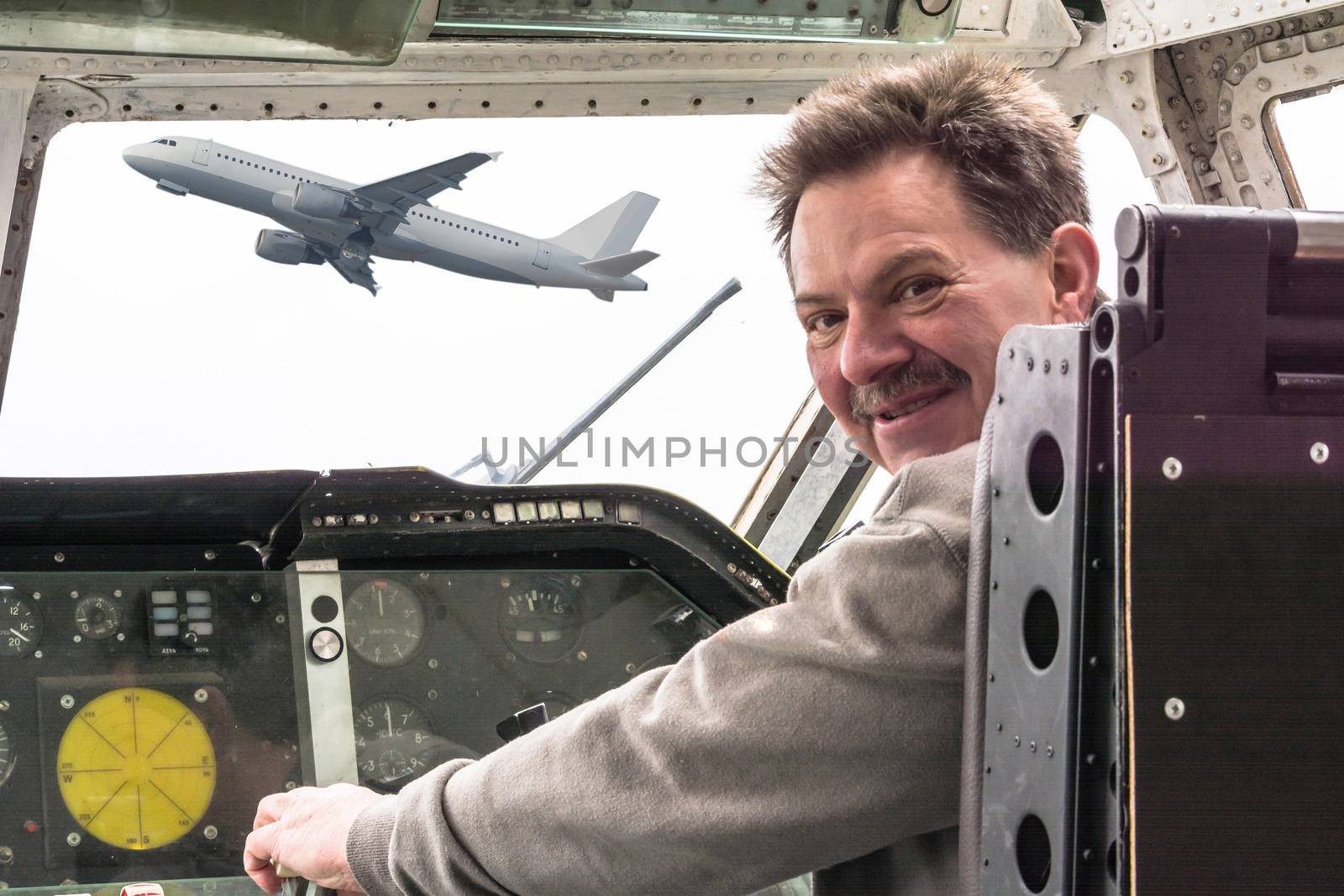 Man in the cockpit. Looking  over his shoulder  smiles , in the background through the cockpit disc see an airplane.