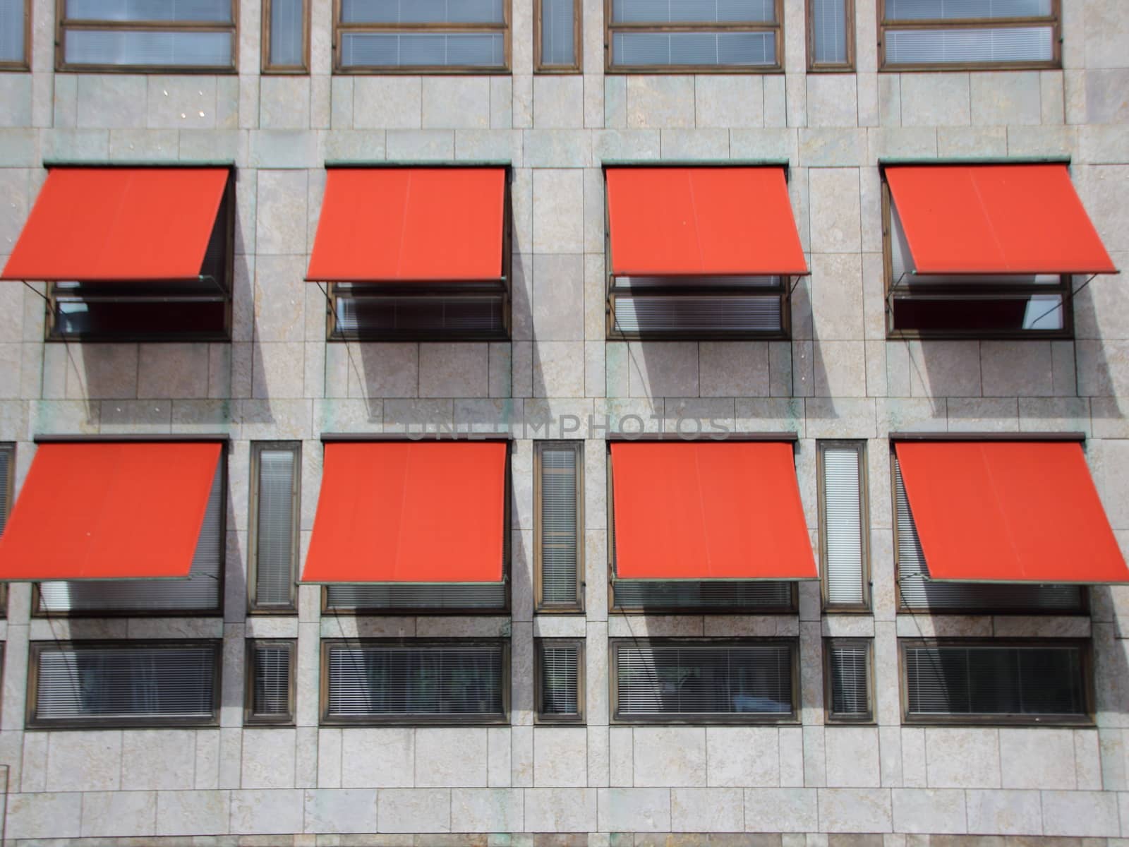 Red Overhang Sunshade Awning with shadows on Grey Building Facade Protecting from the Sun.