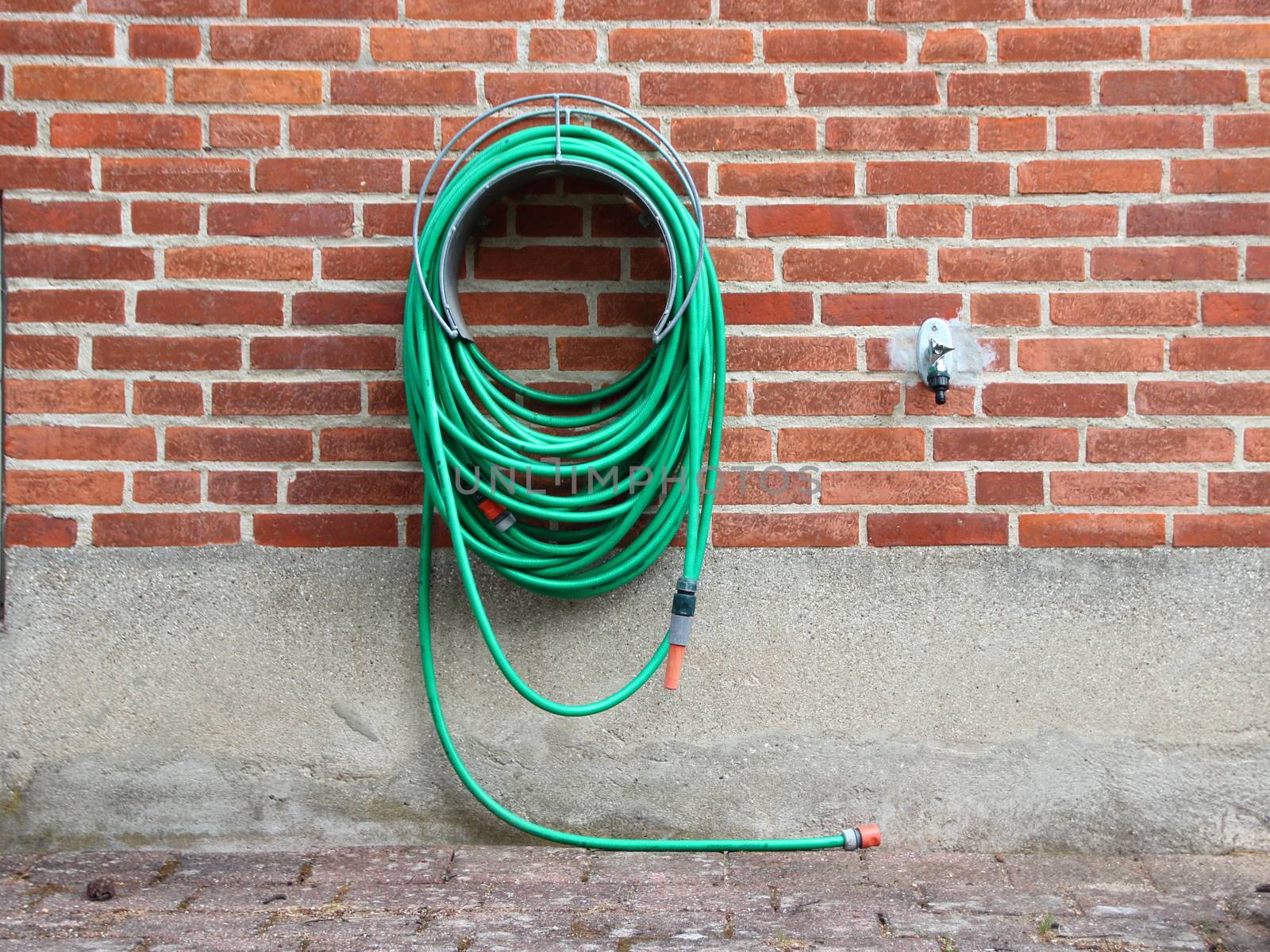 Green Garden Water Hose mounted on Red Brickwall by HoleInTheBox