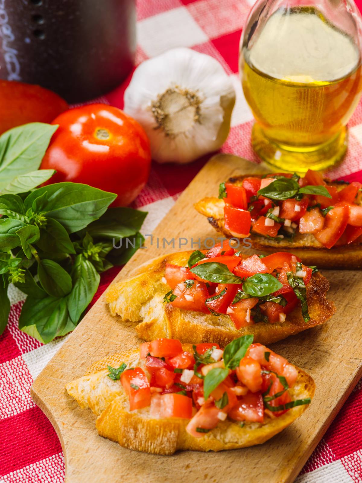 Photo of Italian bruschetta on a wooden board with the ingredients behind. Focus across the middle.
