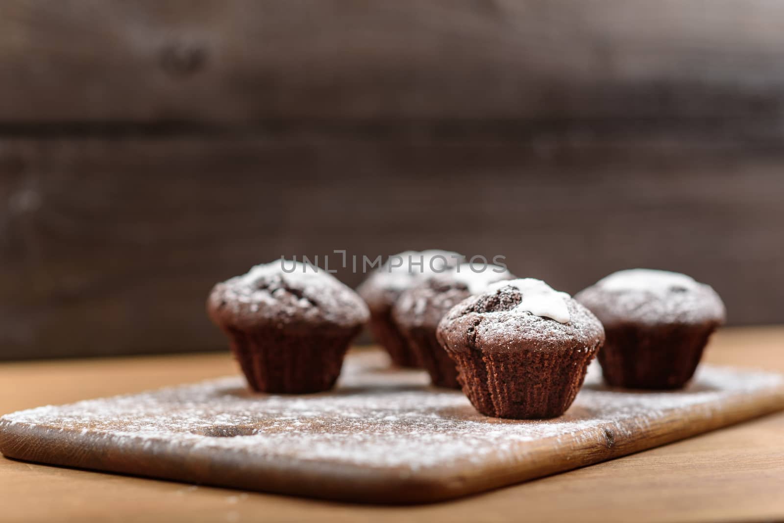 chocolate muffins with white icing lying on a Board sprinkled with powdered sugar