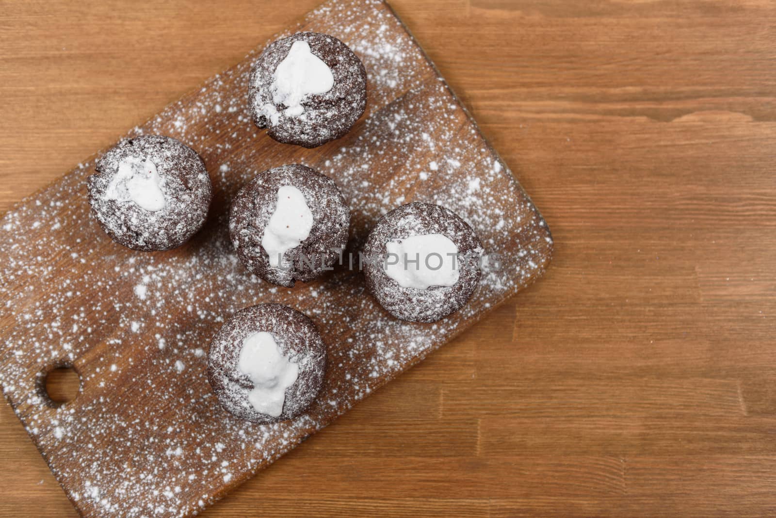 chocolate muffins with white icing lying on a Board sprinkled with powdered sugar