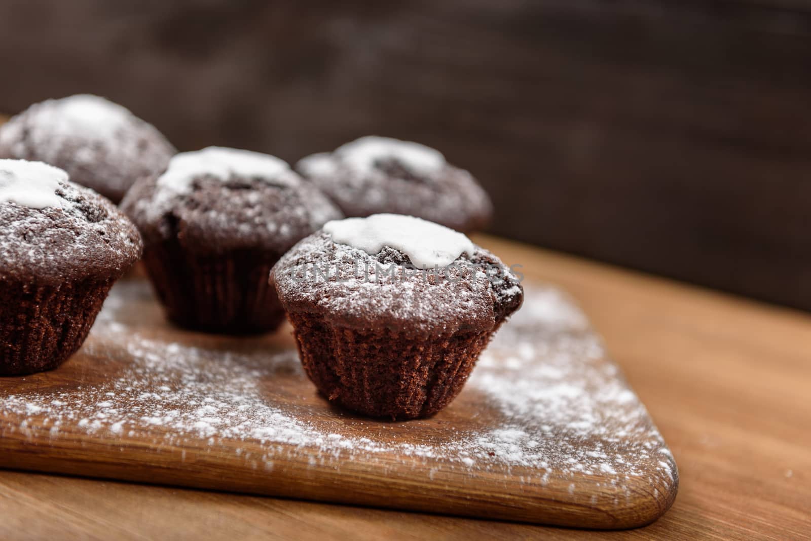 chocolate muffins with white icing lying on a Board sprinkled with powdered sugar