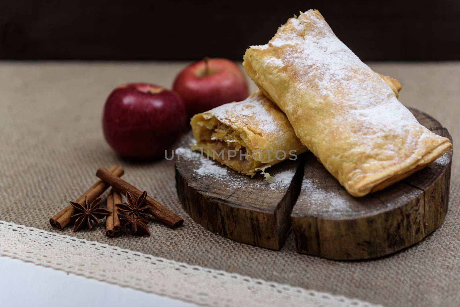 Apple strudel on wooden end of a tree with apples, cinnamon and star anise