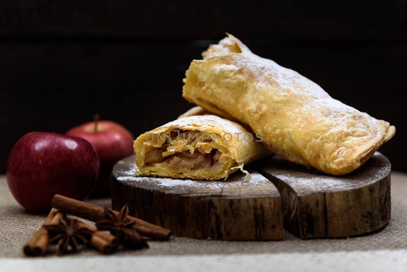 Apple strudel on wooden end of a tree with apples, cinnamon and star anise