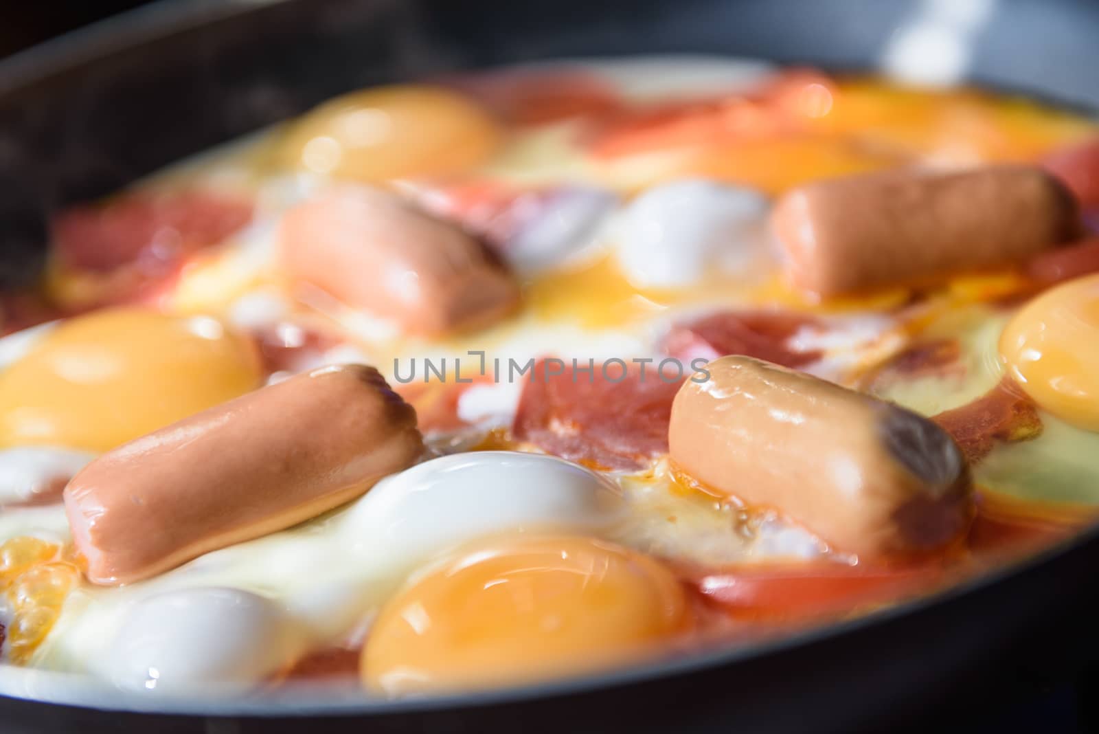 fried eggs with sausages and tomatoes on a hot pan, cooking breakfast