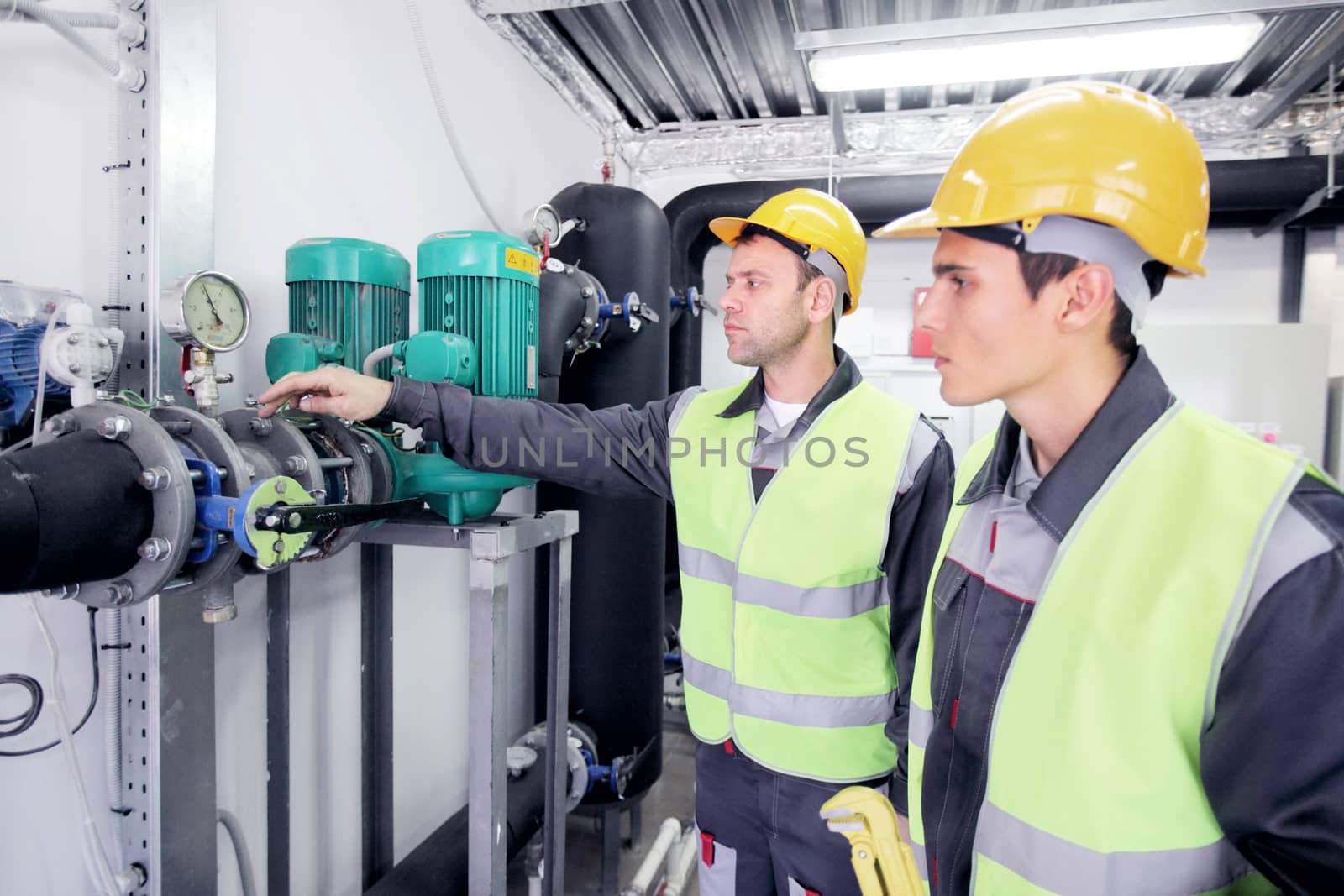 Two workers in hardhats at plant checking parameters of pressure