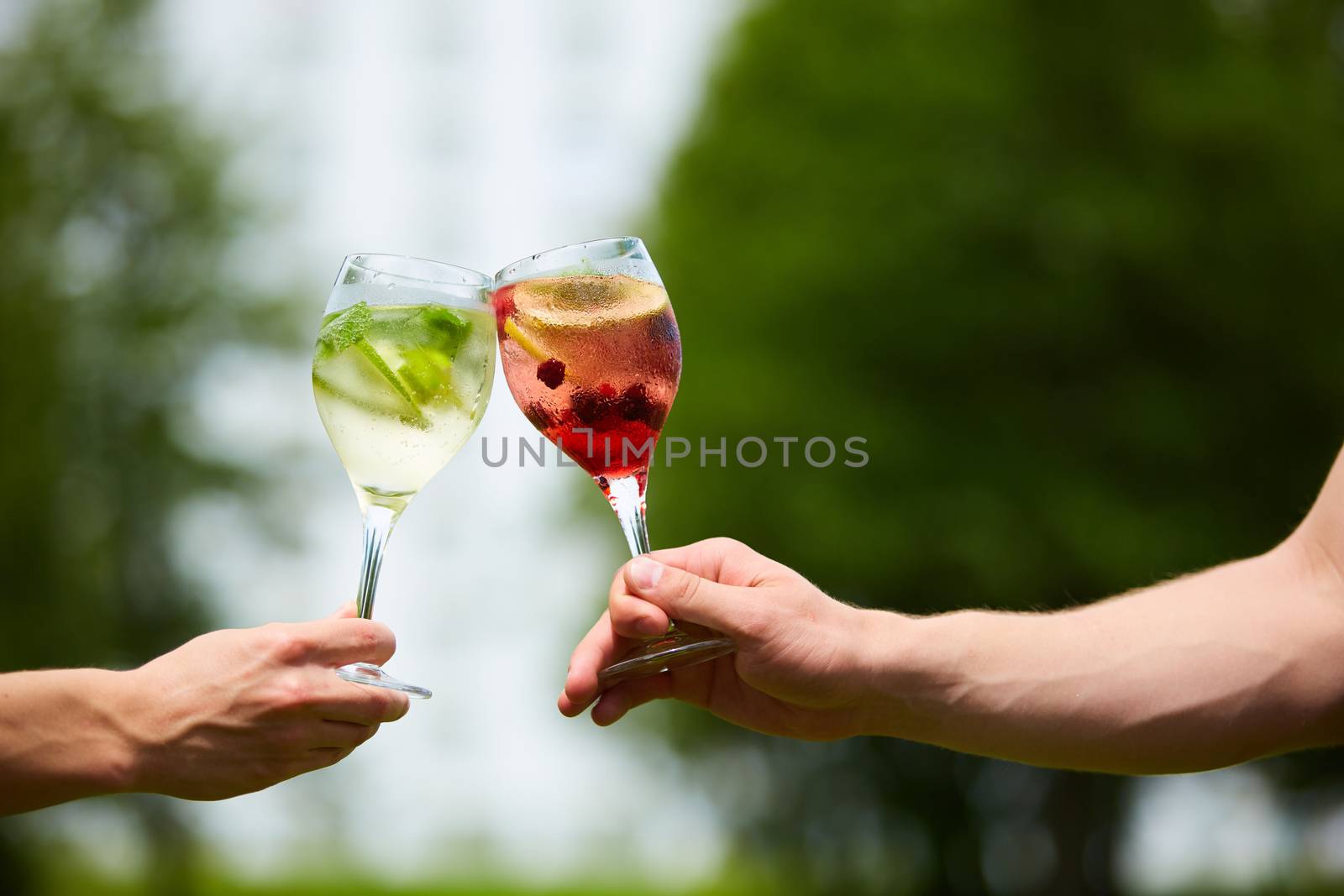 Hand holding glasses of cocktail clinking together at outdoor.