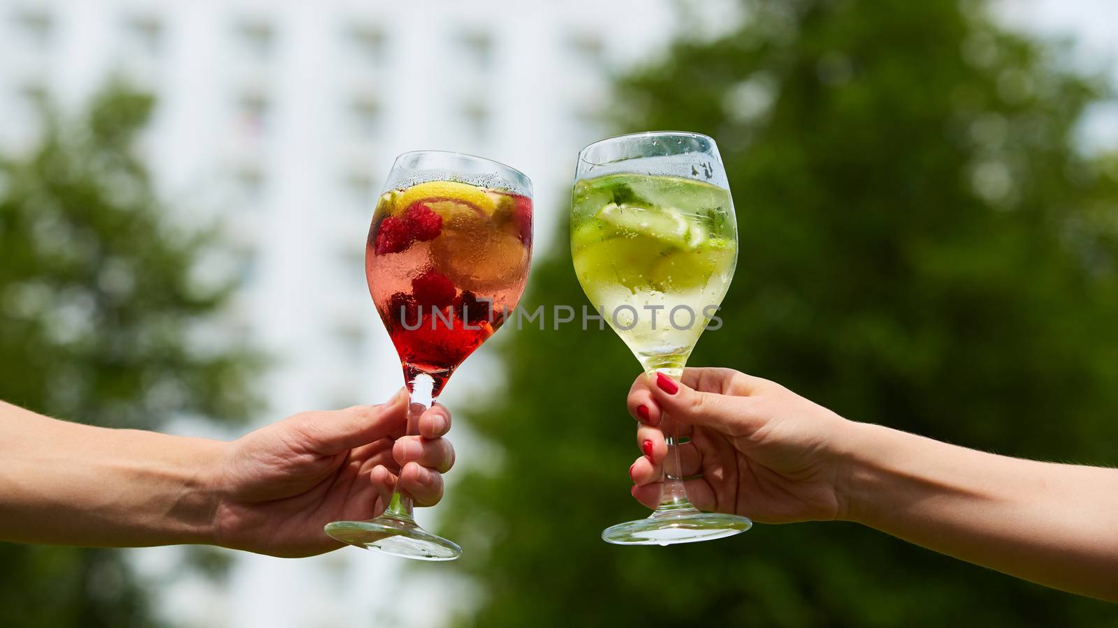 Hand holding glasses of cocktail clinking together at outdoor.
