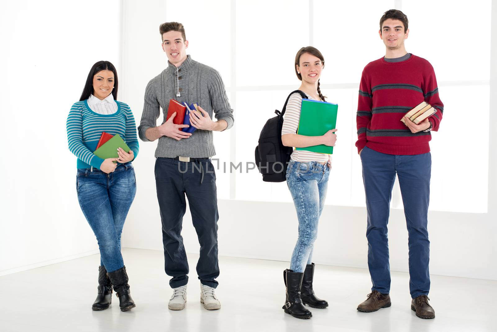 Group of cheerful students with book's standing in school hall and looking at camera.
