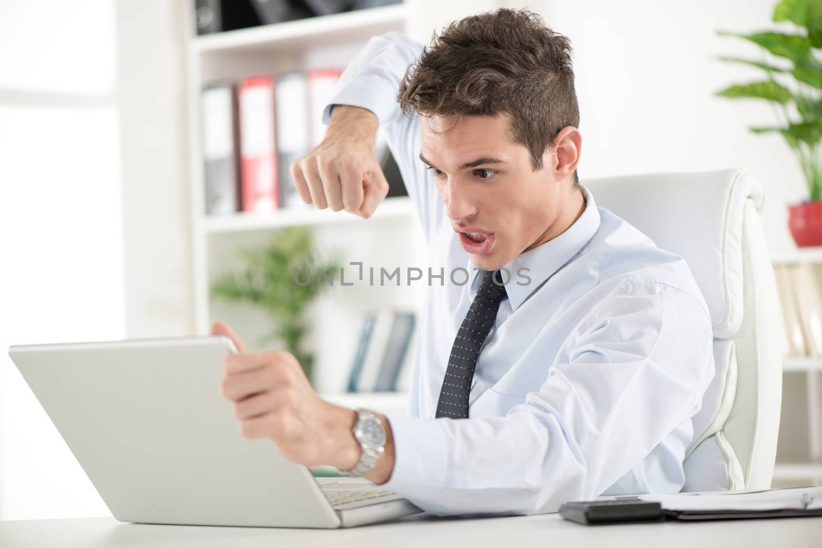 Angry young Businessman sitting in the office and wants to break laptop with fist.