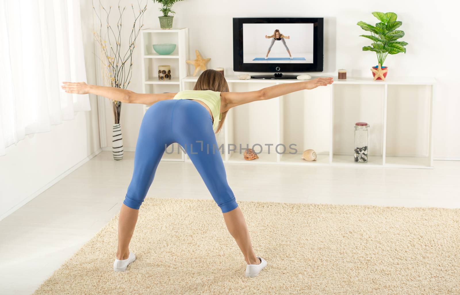 Young woman in sports clothes, doing exercises in the room, in front TV.