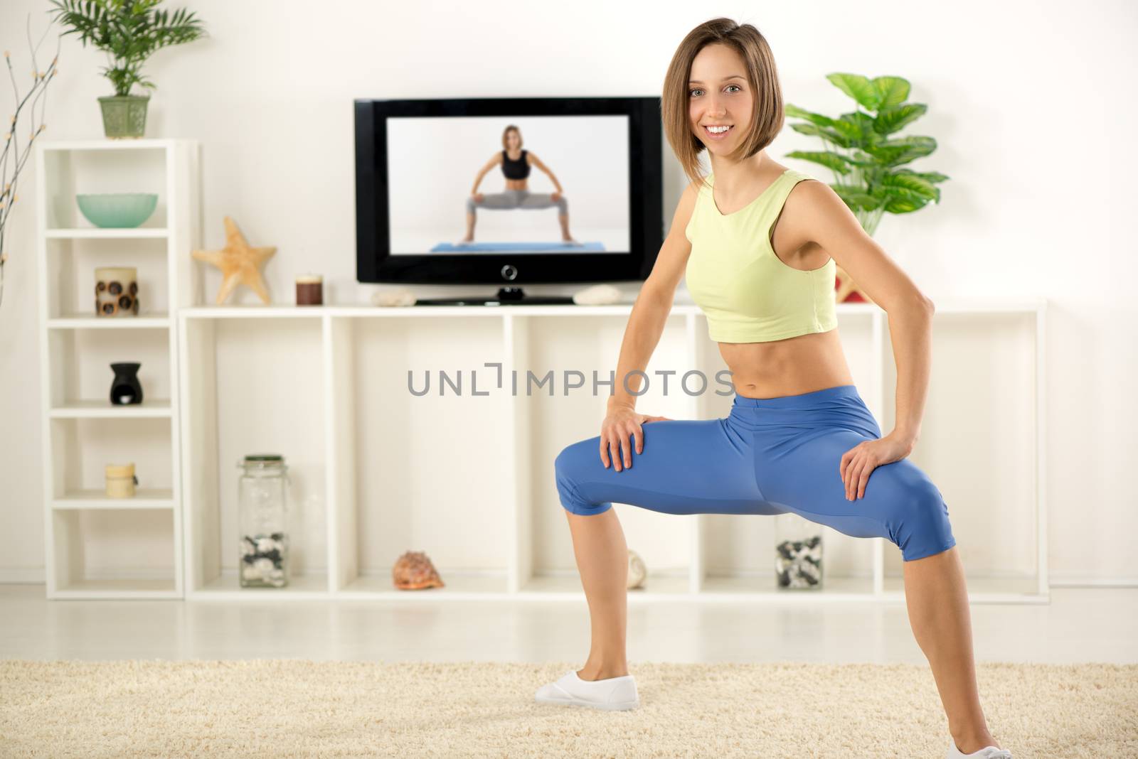Young woman in sports clothes, doing exercises in the room, in front TV.