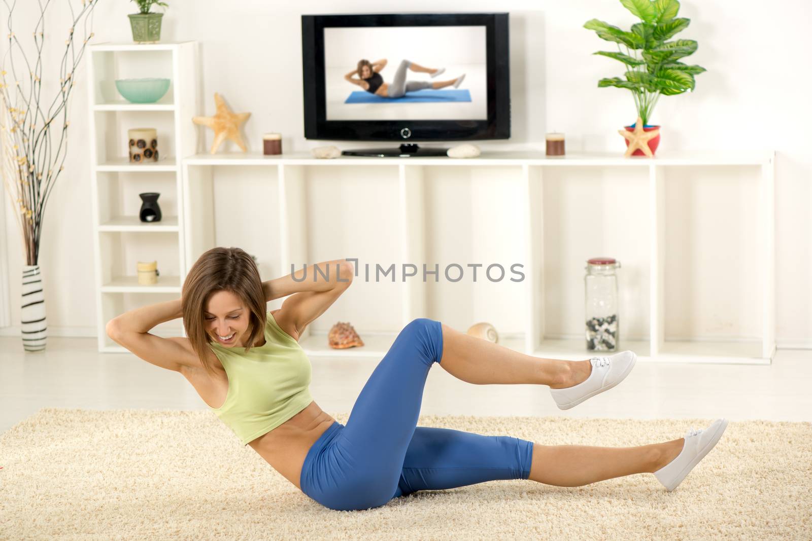 Young woman in sports clothes, doing exercises in the room, in front TV.