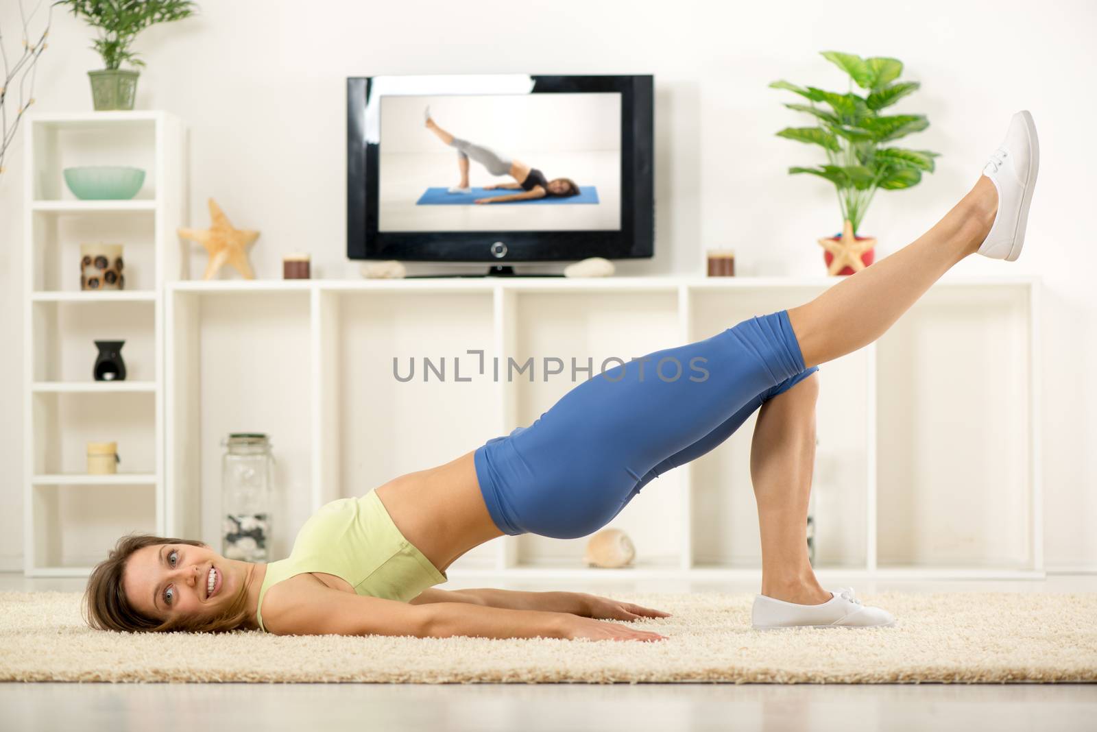 Young woman in sports clothes, doing exercises in the room, in front TV.