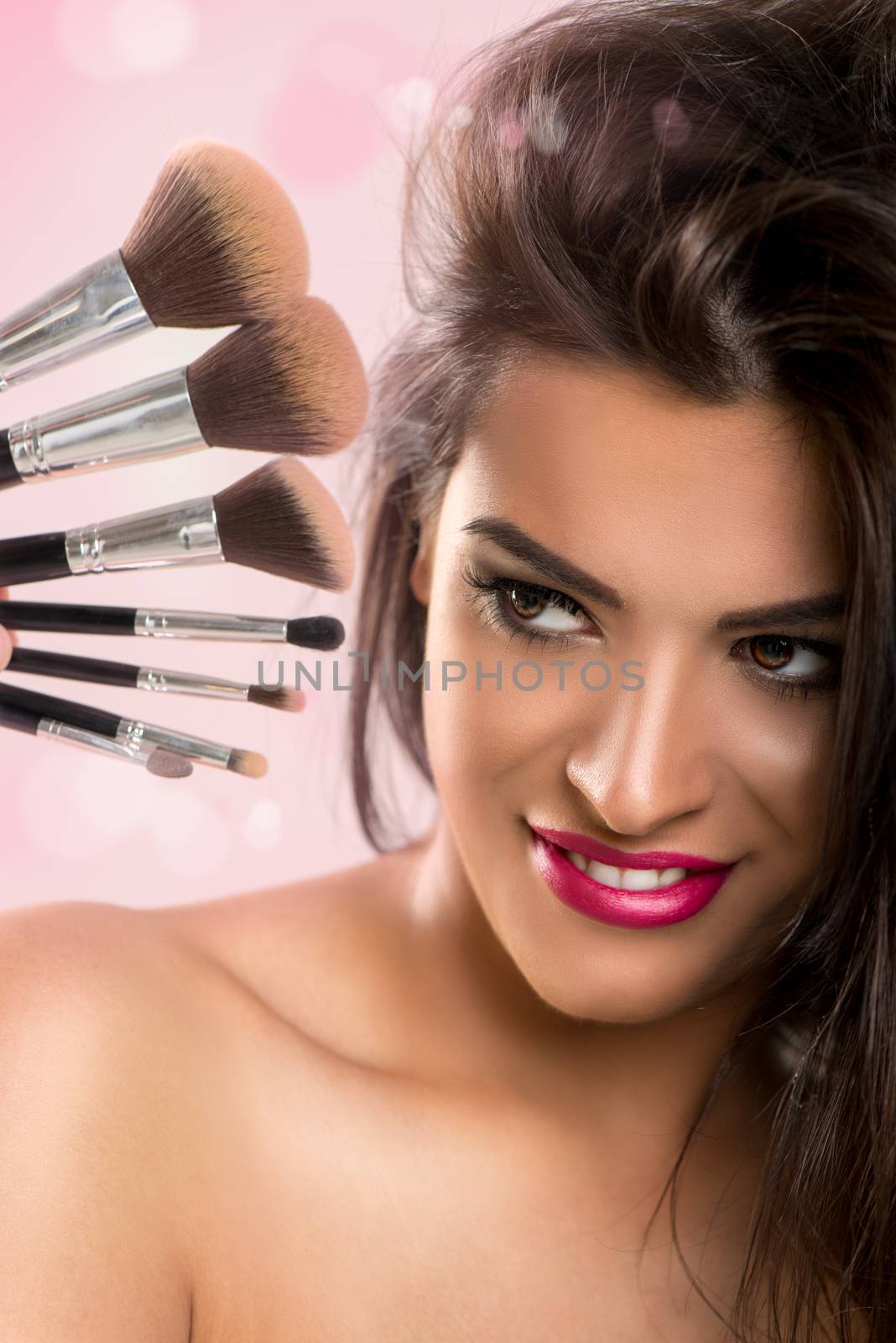 Portrait of a cute young brunette woman with set make-up brushes.