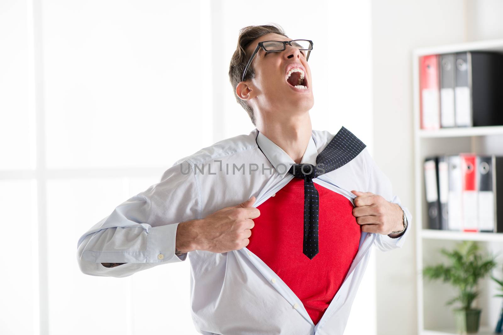 Angry businessman ripping open his shirt and exposing a Superhero red costume underneath. The man is wearing glasses.