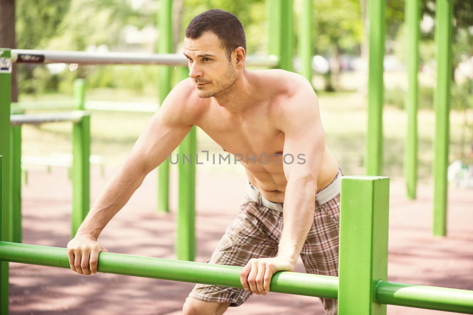 Naked muscle man resting after exercising in the outdoor gym.
