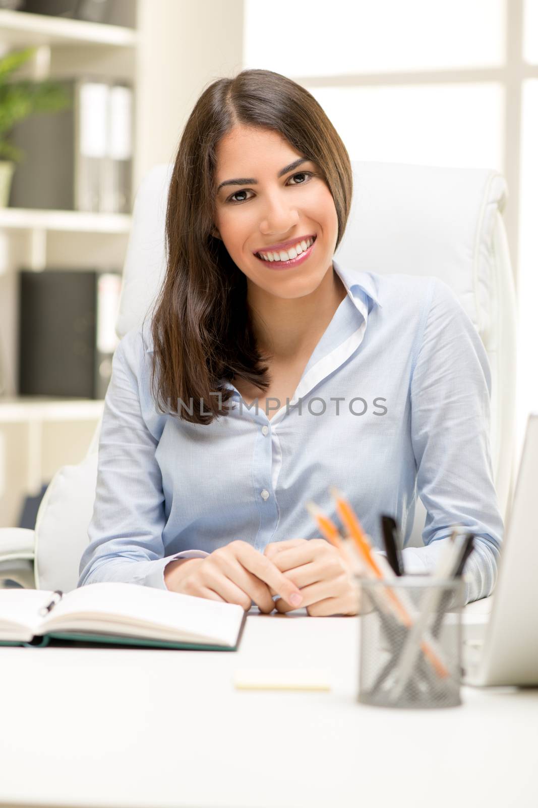 Portrait of a beautiful young businesswoman sitting in the office, smiling and looking at camera.