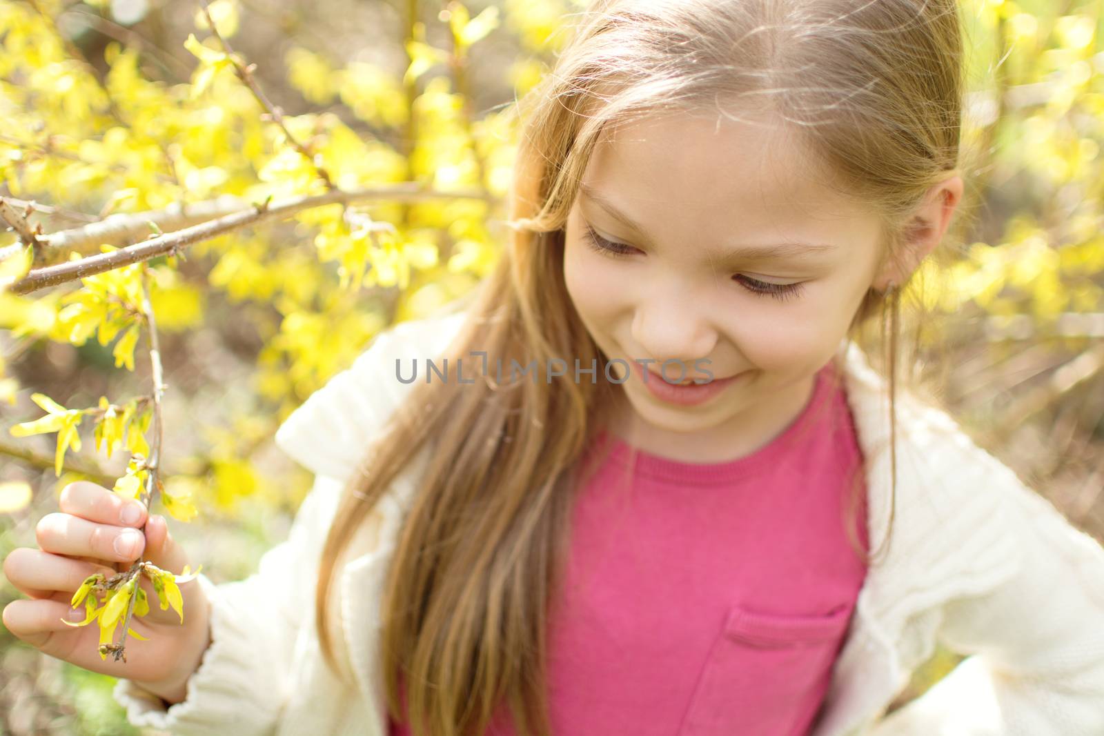 Smiling cute little girl standing beside a flower tree in the park and thinking.