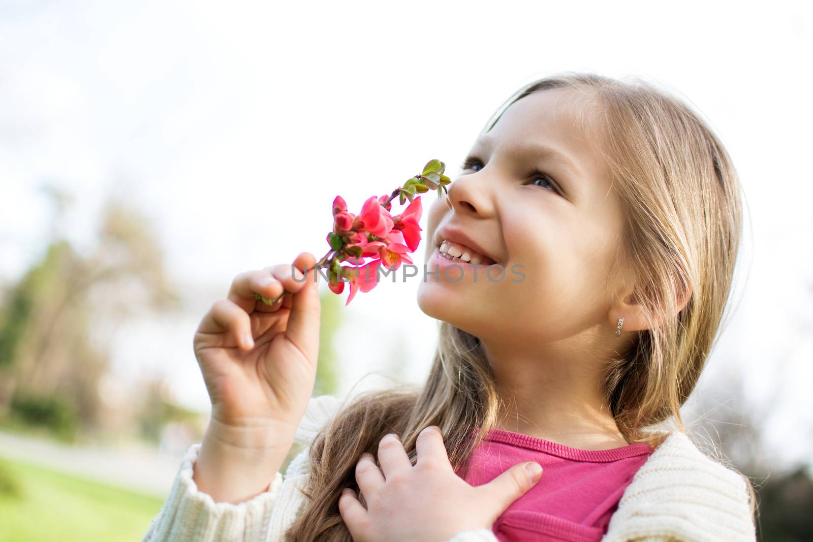 Smiling cute little girl smelling spring flower in the park.
