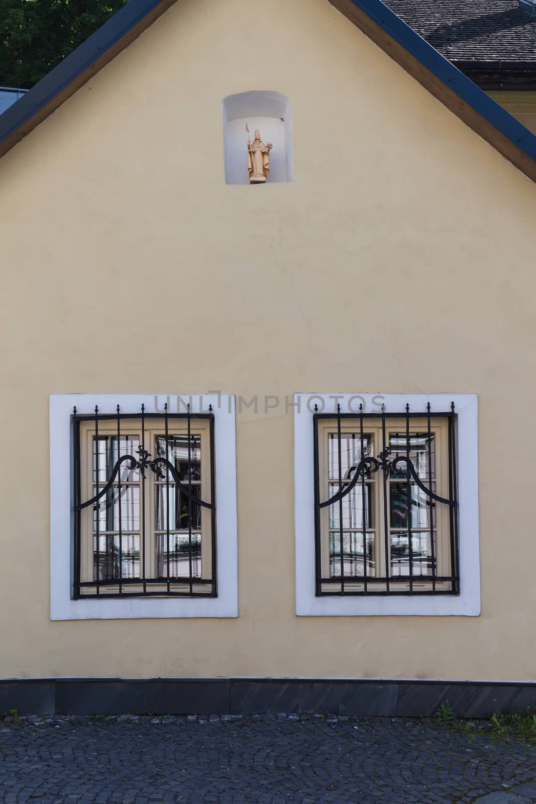 Facade of an old renewed house in medieval city Banska Stiavnica, Slovakia. Two windows with white frames and a saint statue.