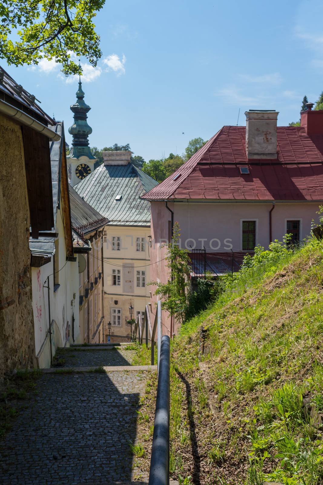 Small street on a hill in the medieval city Banska Stiavnica, Slovakia. Old houses and a tower of a church. Blue summer sky with some clouds.