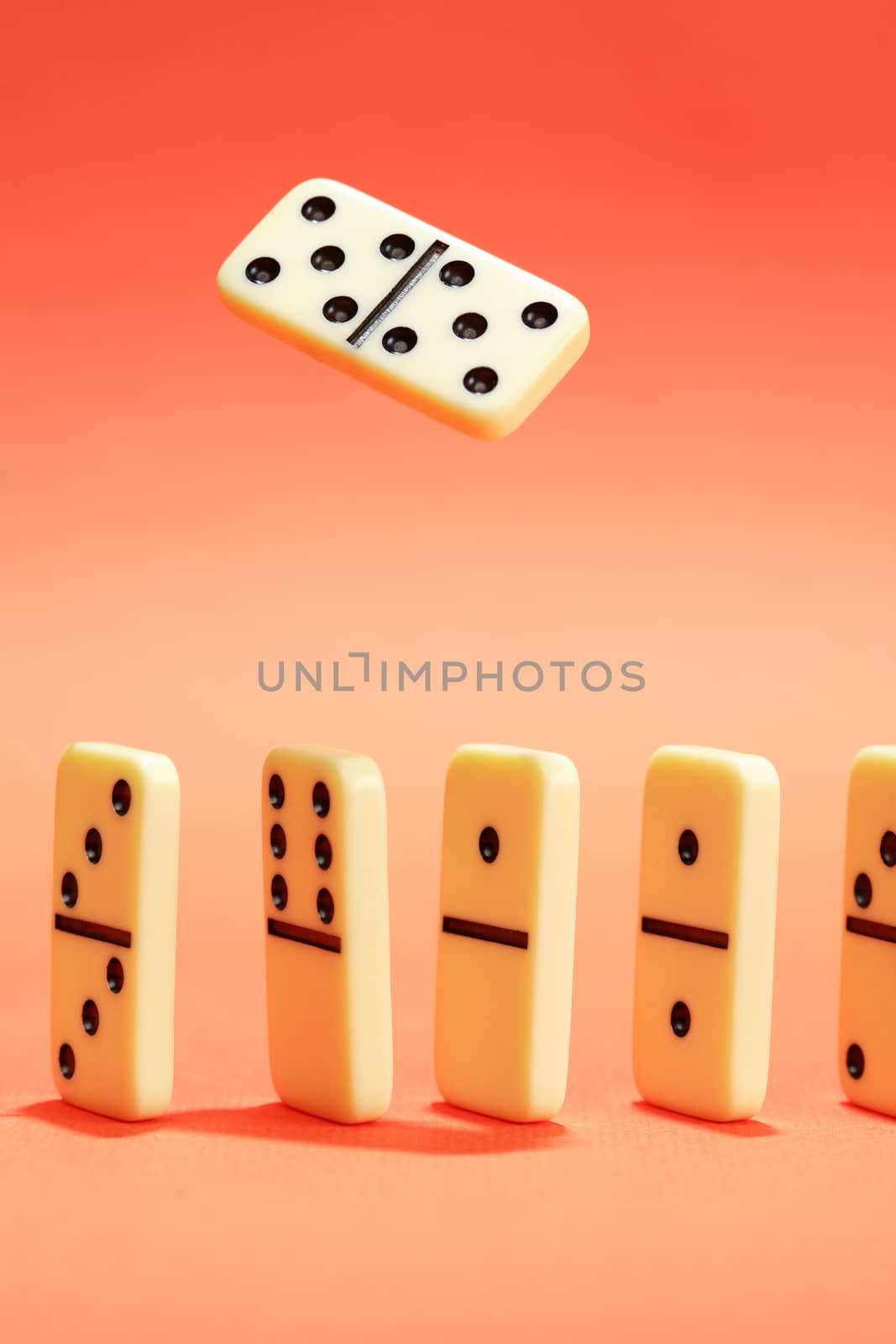 White dominoes standing in a row on red background. One domino above