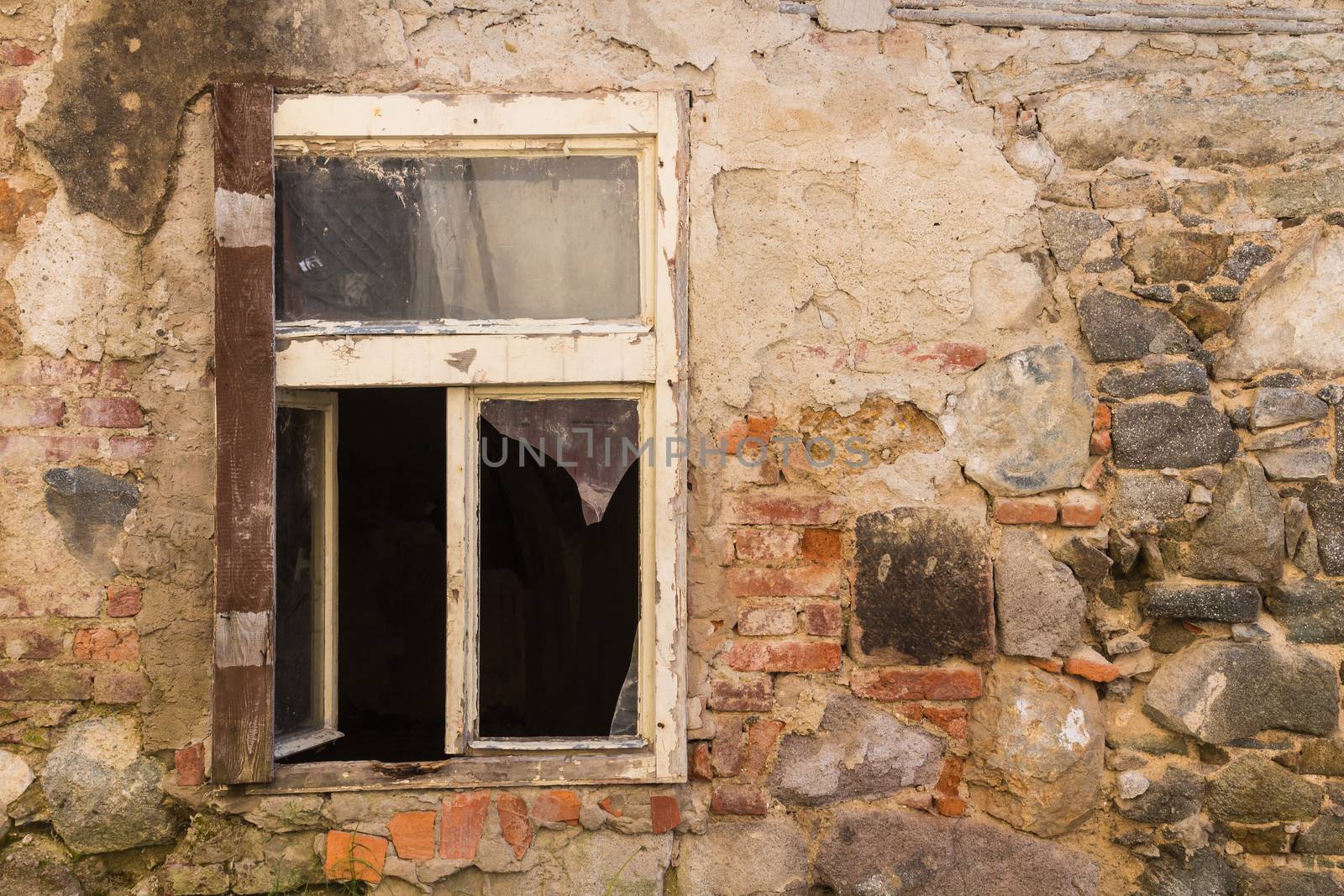 Window of an abandoned house. Broken glass. Wall of the building with many details of the colorful bricks and stones.