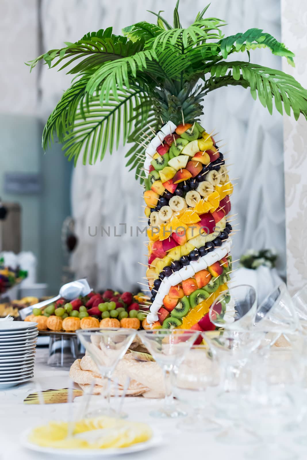 Palm tree decorated with exotic fruits on sticks stands on the wedding