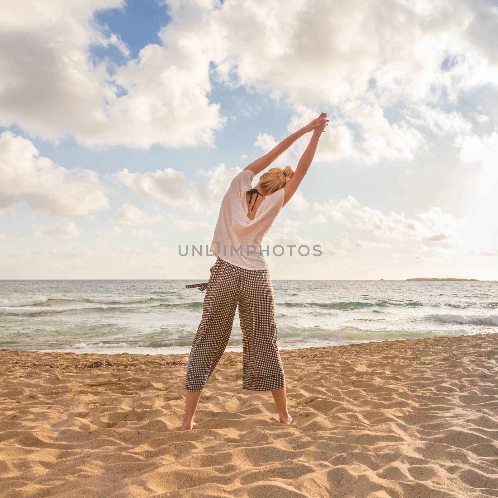Active young woman practicing yoga on beach at sunset.