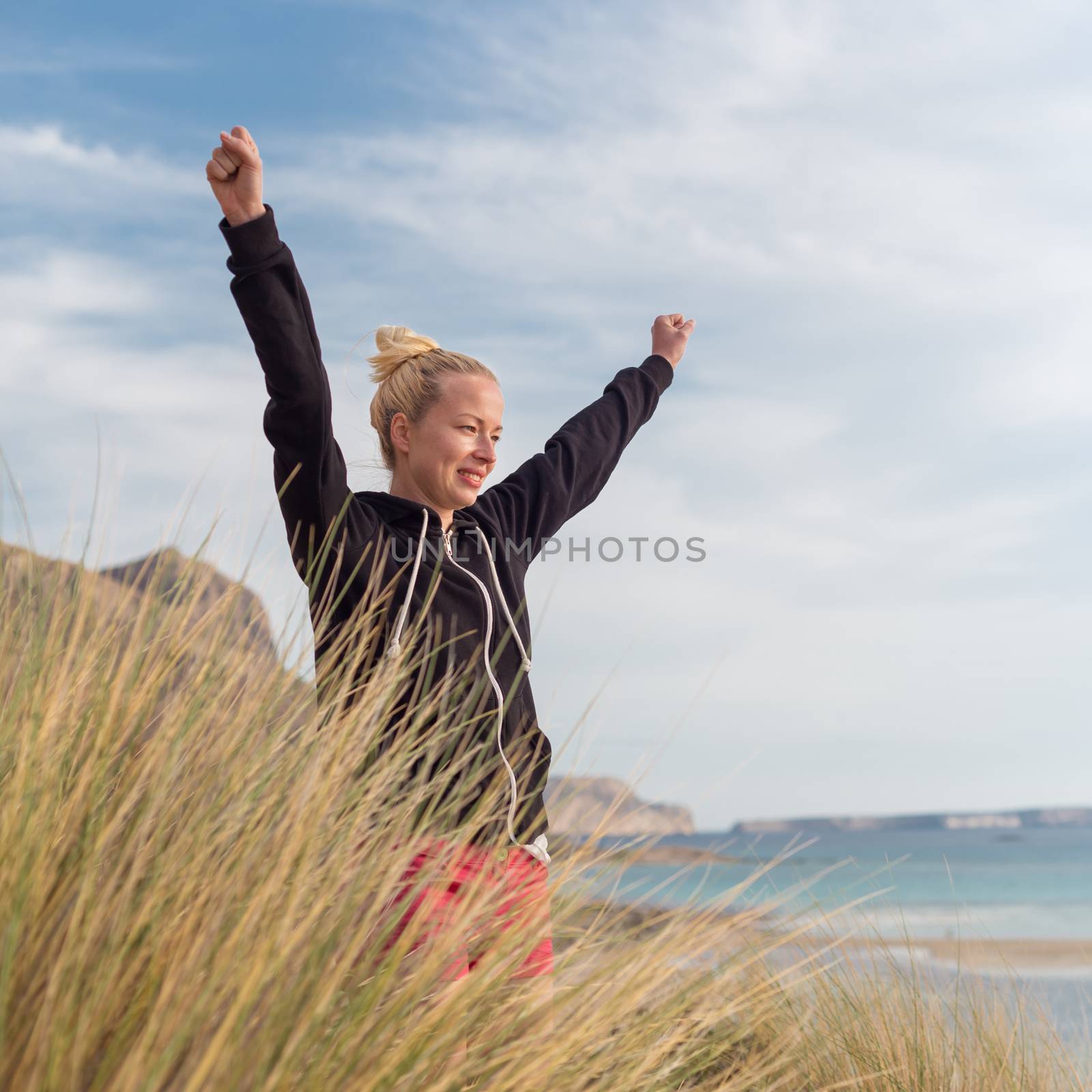 Active sporty woman, arms rised, enjoying sun, freedom and life an a beautiful beach. Young lady feeling free, relaxed and happy. Active lifestyle outdoors. Made it.