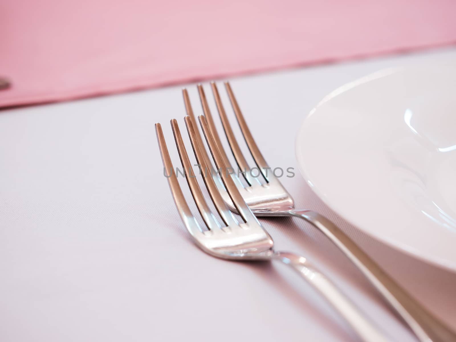 Two kitchen forks on dinner table with pink tablecloth