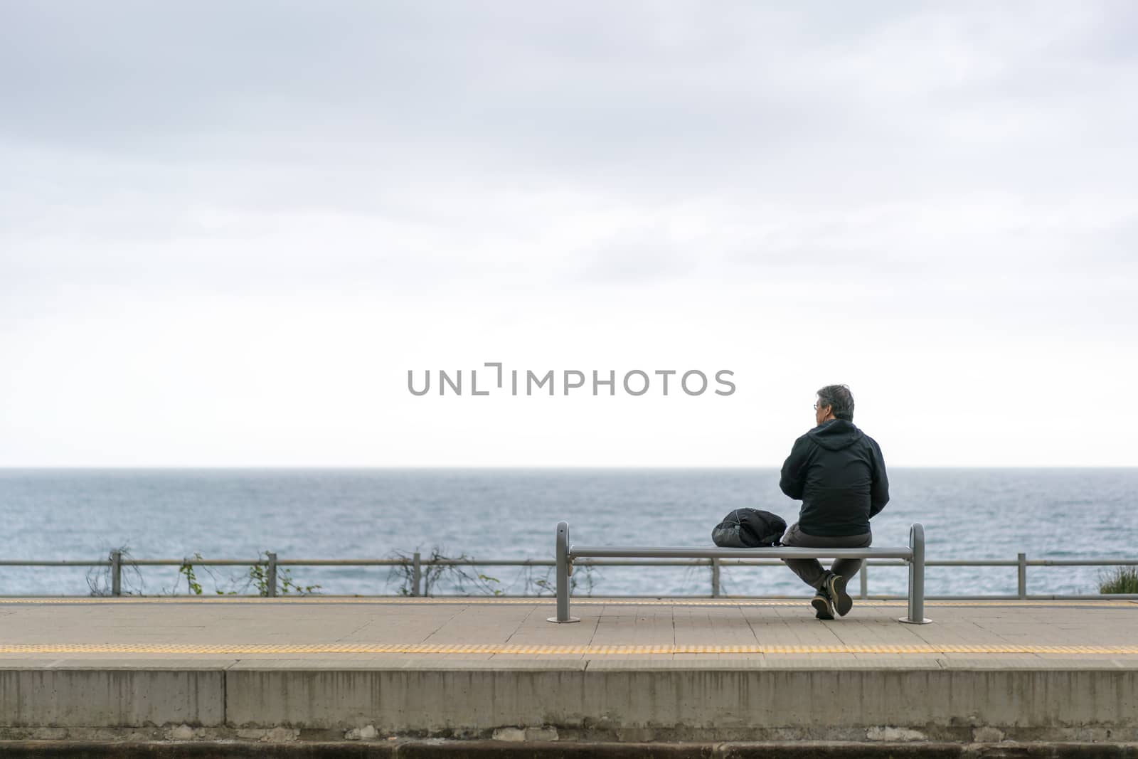 Corniglia, Italy - Apr 8, 2016: Unidentified backpacker old man tourist wait for train by the ocean with gloomy sky background, looking at copy space, at Corniglia train station, Cinque Terre, Italy by beer5020