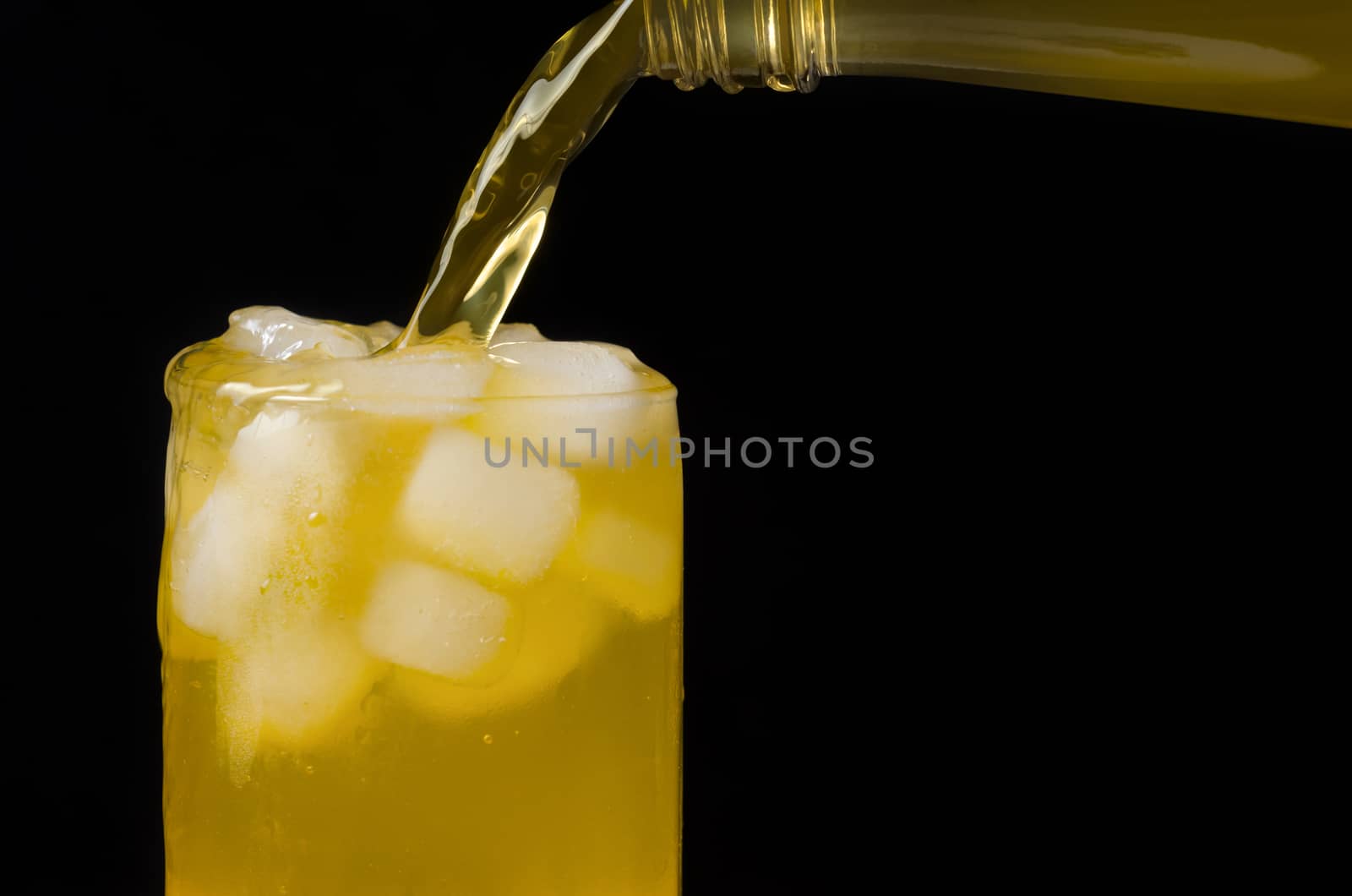 The lemonade poured over the edge ,from a bottle into a glass with ice. Black background.
