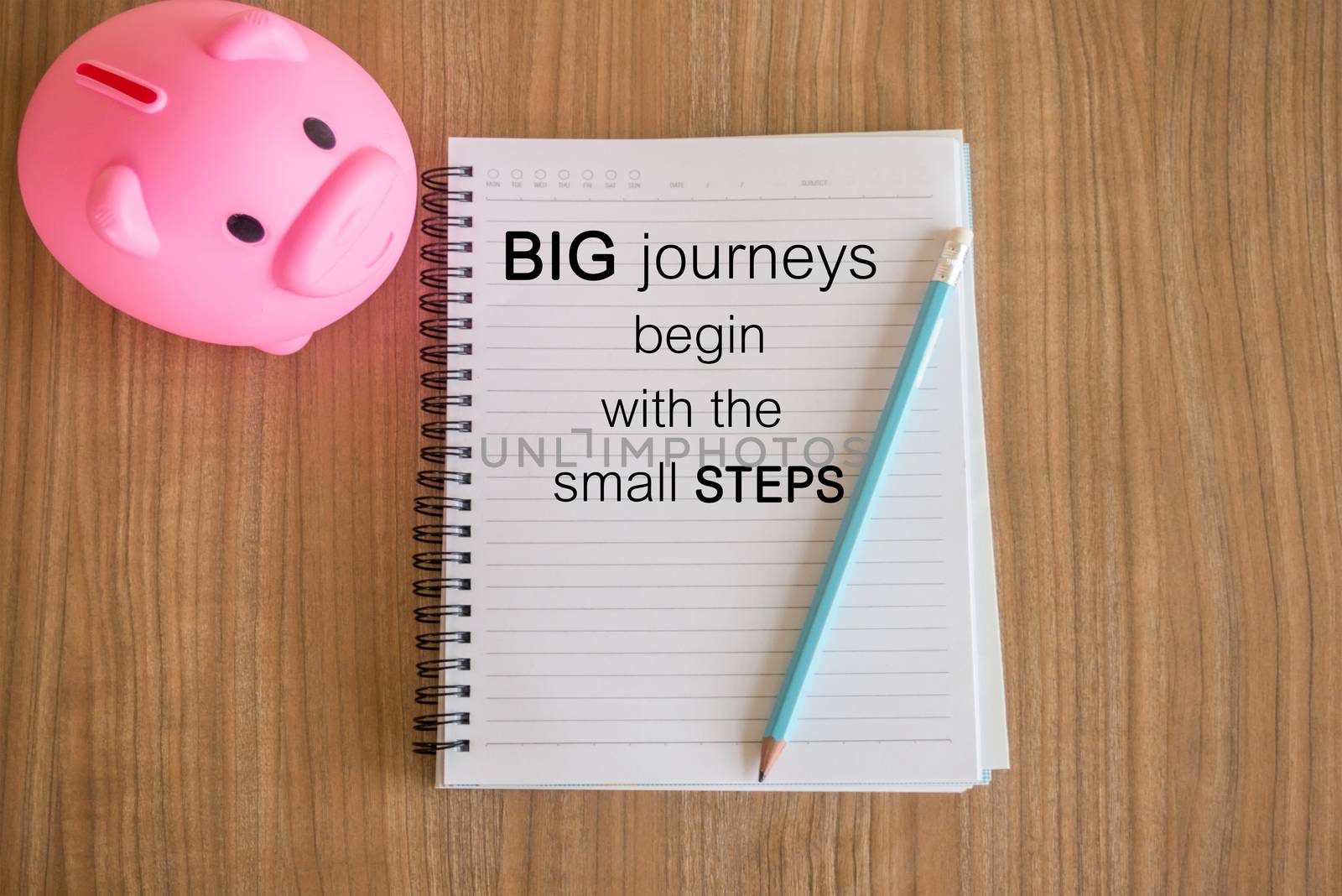 Word  Big journeys begin with the small steps.Inspirational motivational quote on paper and a piggy bank on the wooden table background