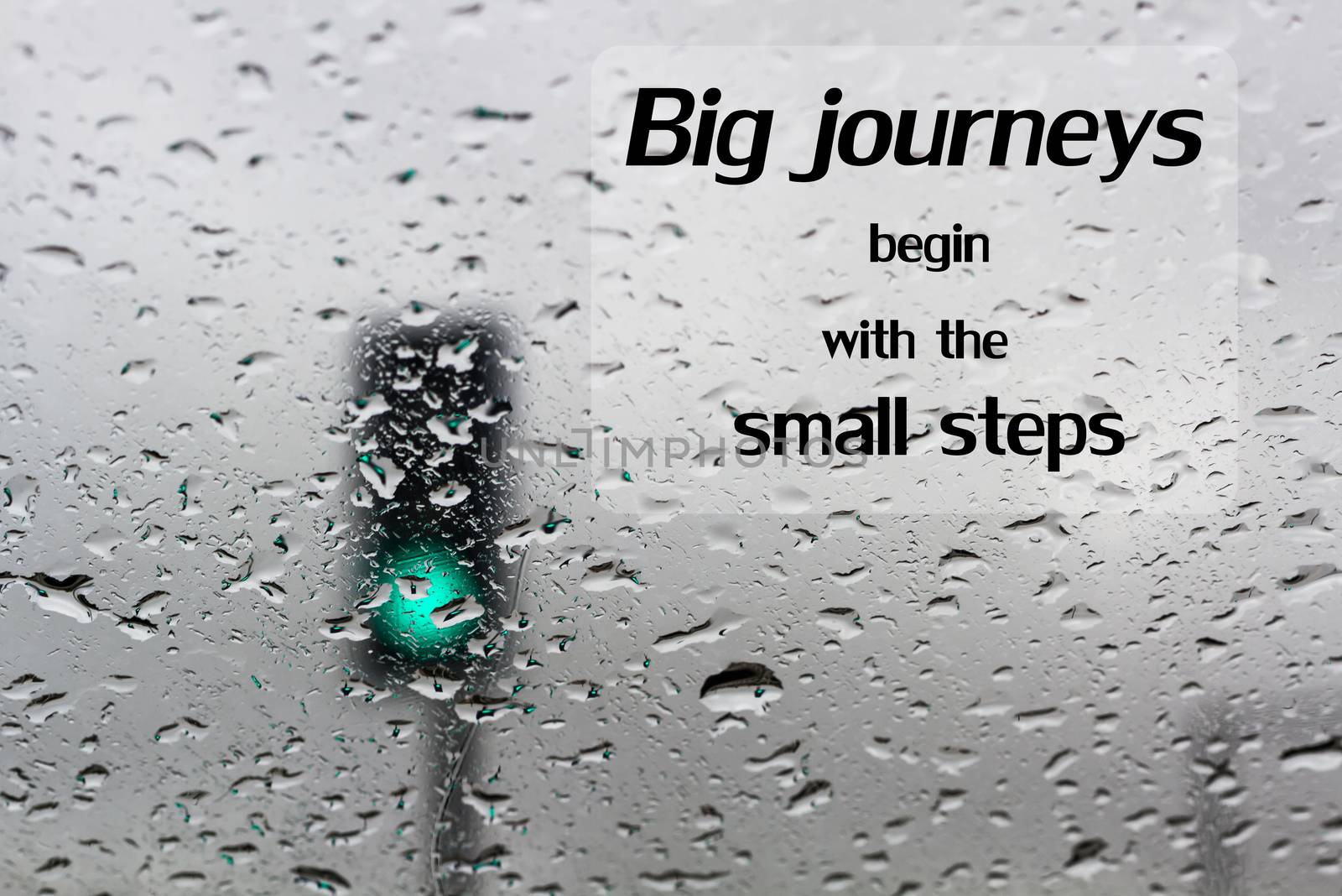 Word  Big journeys begin with the small steps.Inspirational motivational quote on traffic light on a rainy day window background