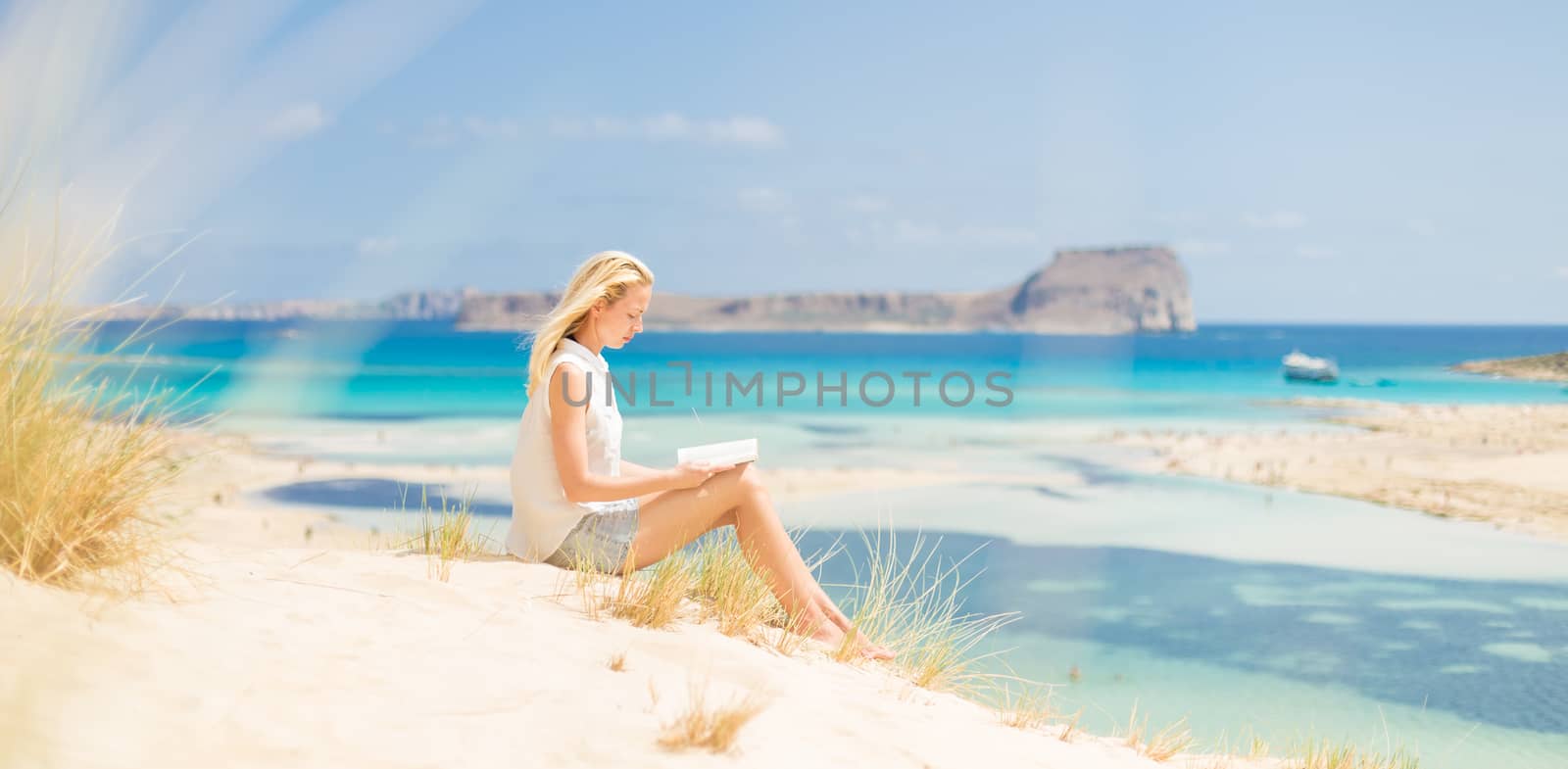 Woman reading book, enjoying sun on beach. by kasto