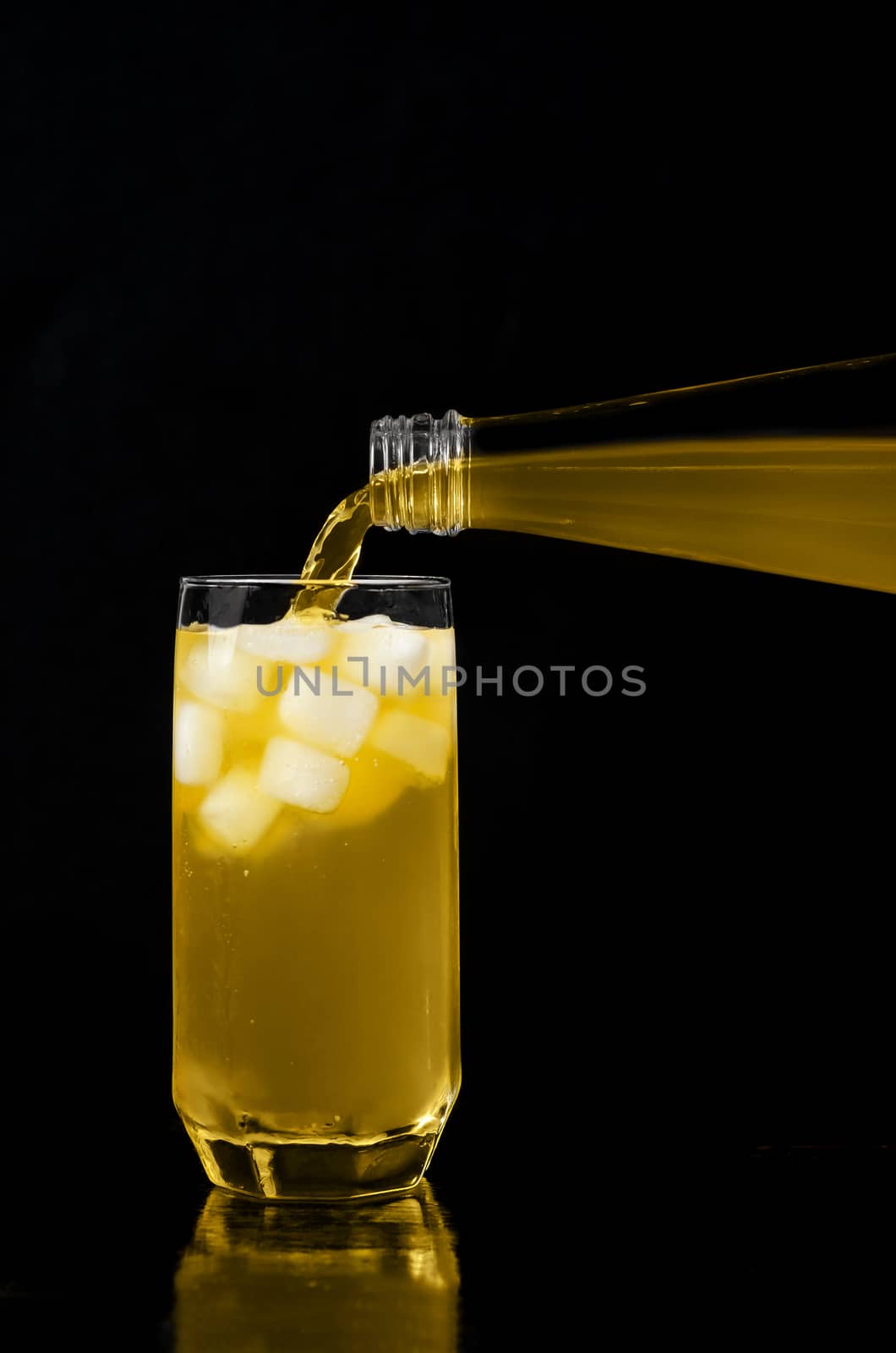 Lemonade pouring from bottle into glass with ice. Black background.