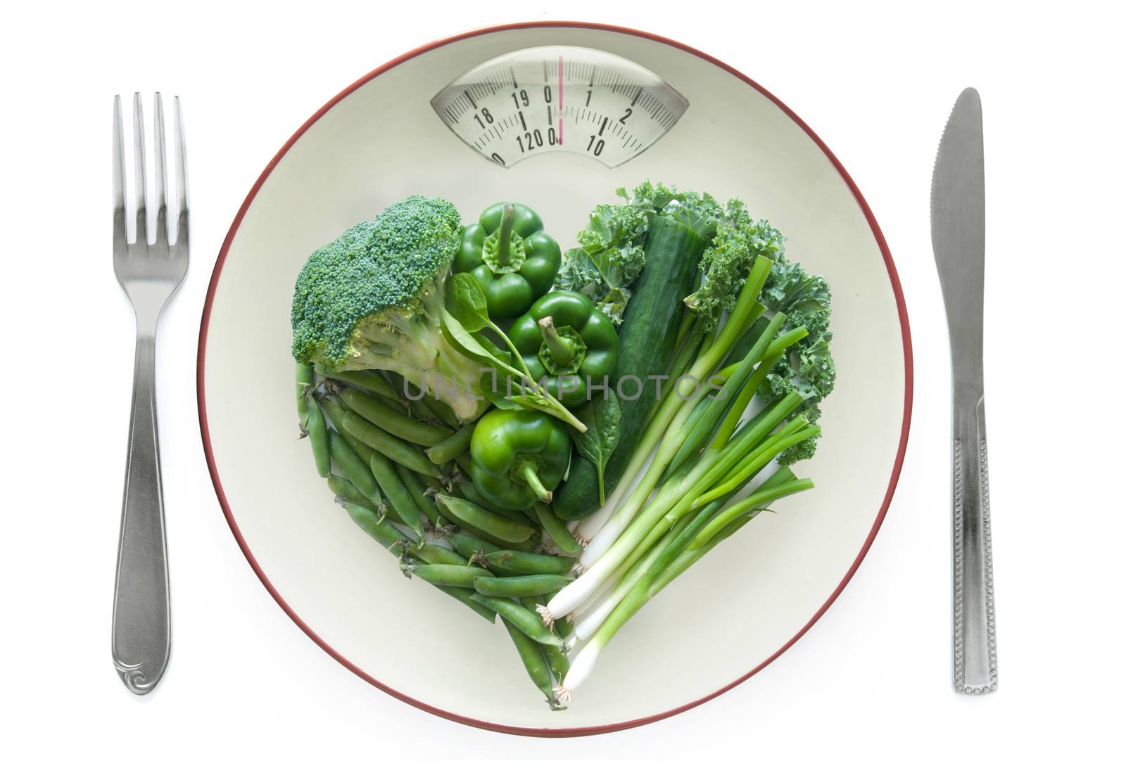 Weighing scales plate with green vegetables over a white background