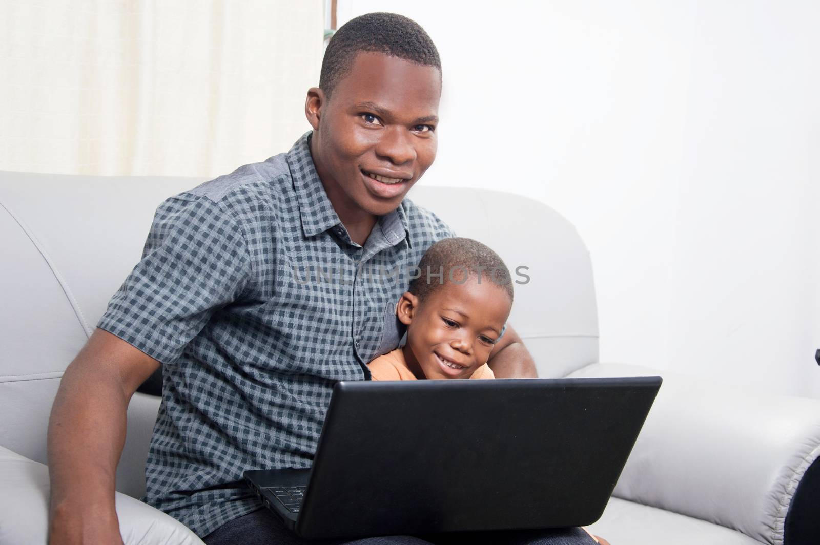 The child is concentrated on the laptop while his father watched the camera.