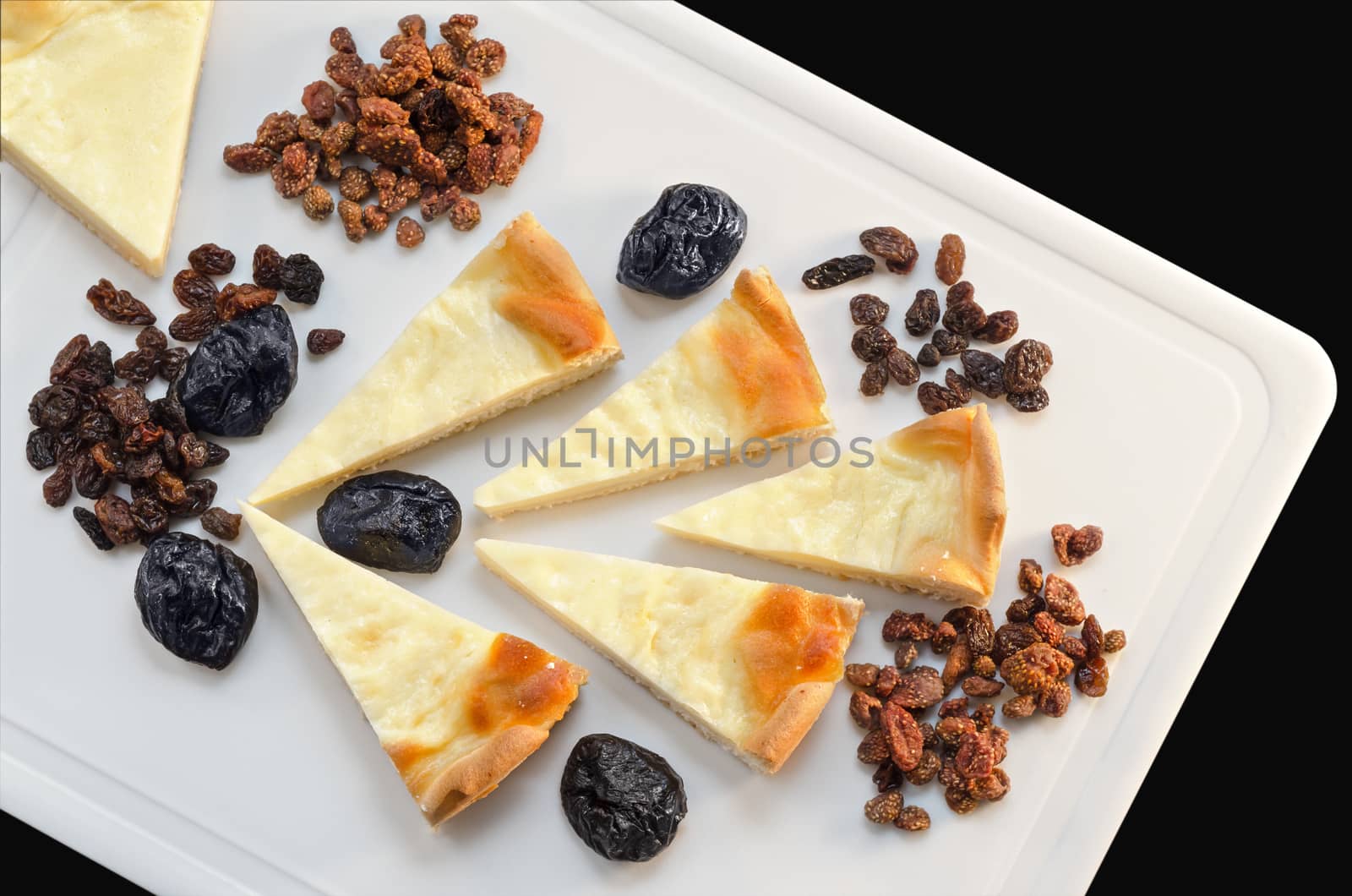 Slices of sour cream cake and dried fruit lying on a white cutting Board, isolated on black background