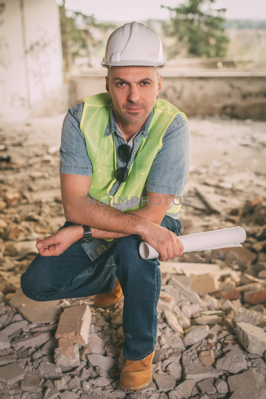 Construction architect holding plans and looking at camera in building damaged in the disaster.
