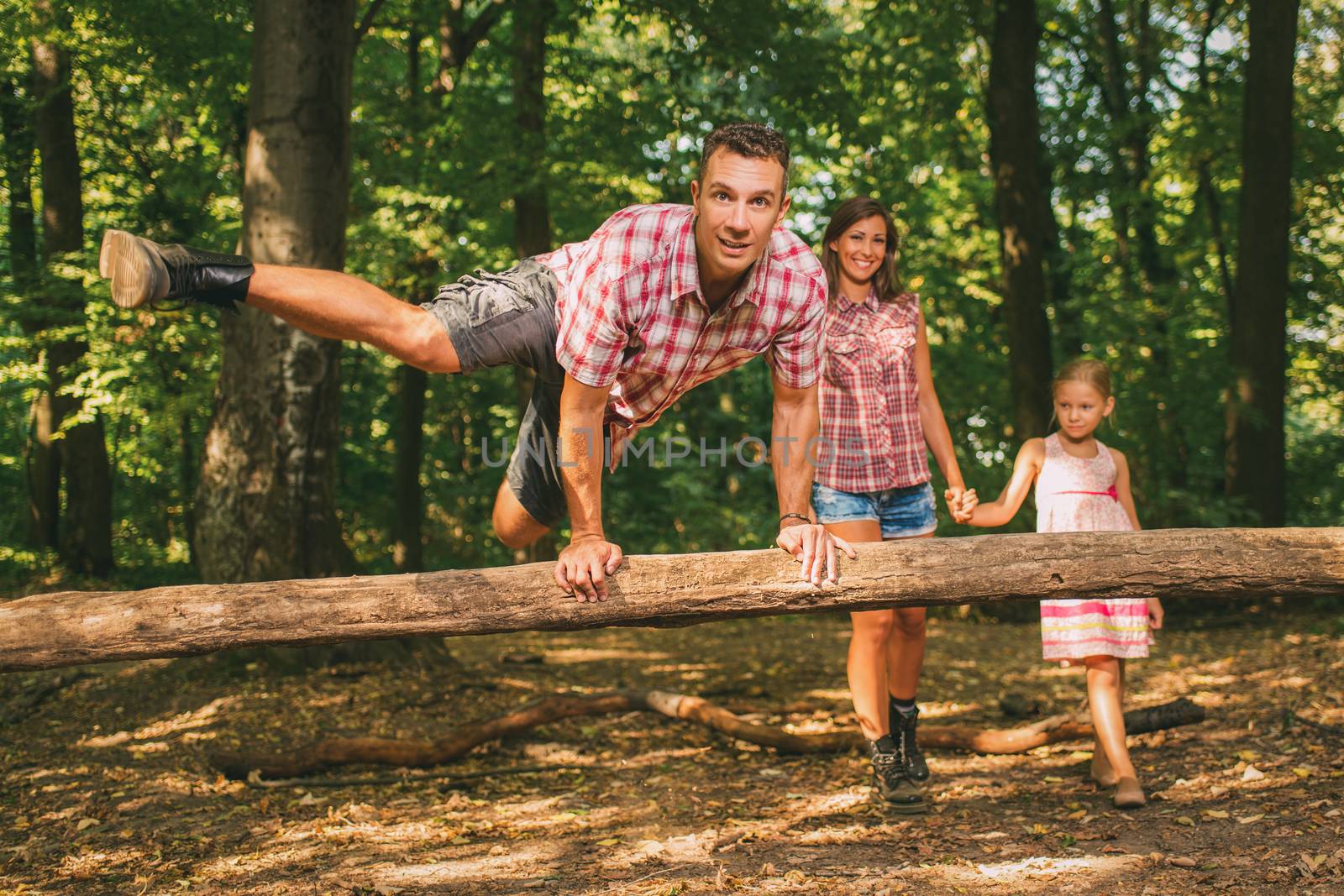 Beautiful young family having fun while walking through the forest.