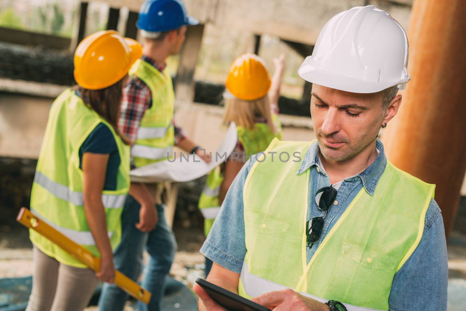 Construction architects using digital tablet in building damaged in the disaster. His colleagues review plan.